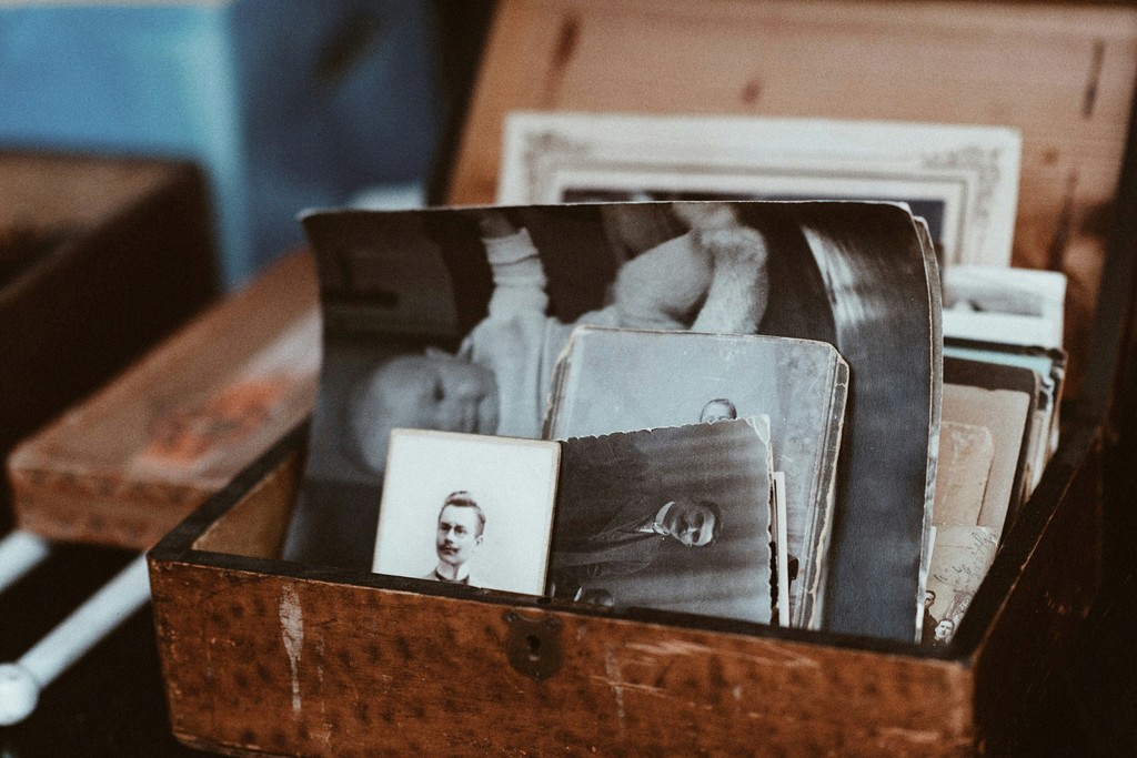 A wooden box filled with vintage black-and-white photographs, including portraits of men from the early 20th century. The collection, showcasing old-fashioned attire and formal poses, highlights the preservation of family history and the timelessness of cherished memories.