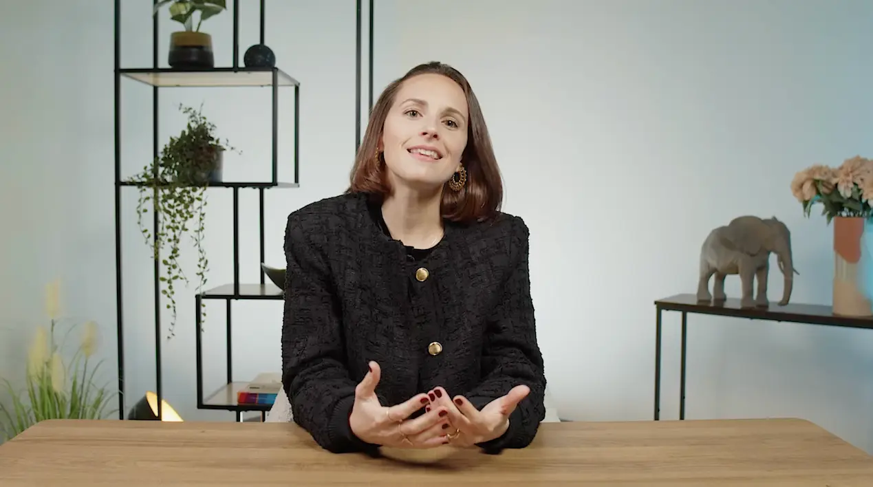 Femme assise à un bureau dans un studio lumineux, en train d’expliquer un sujet lié au stress, au sommeil et aux habitudes alimentaires