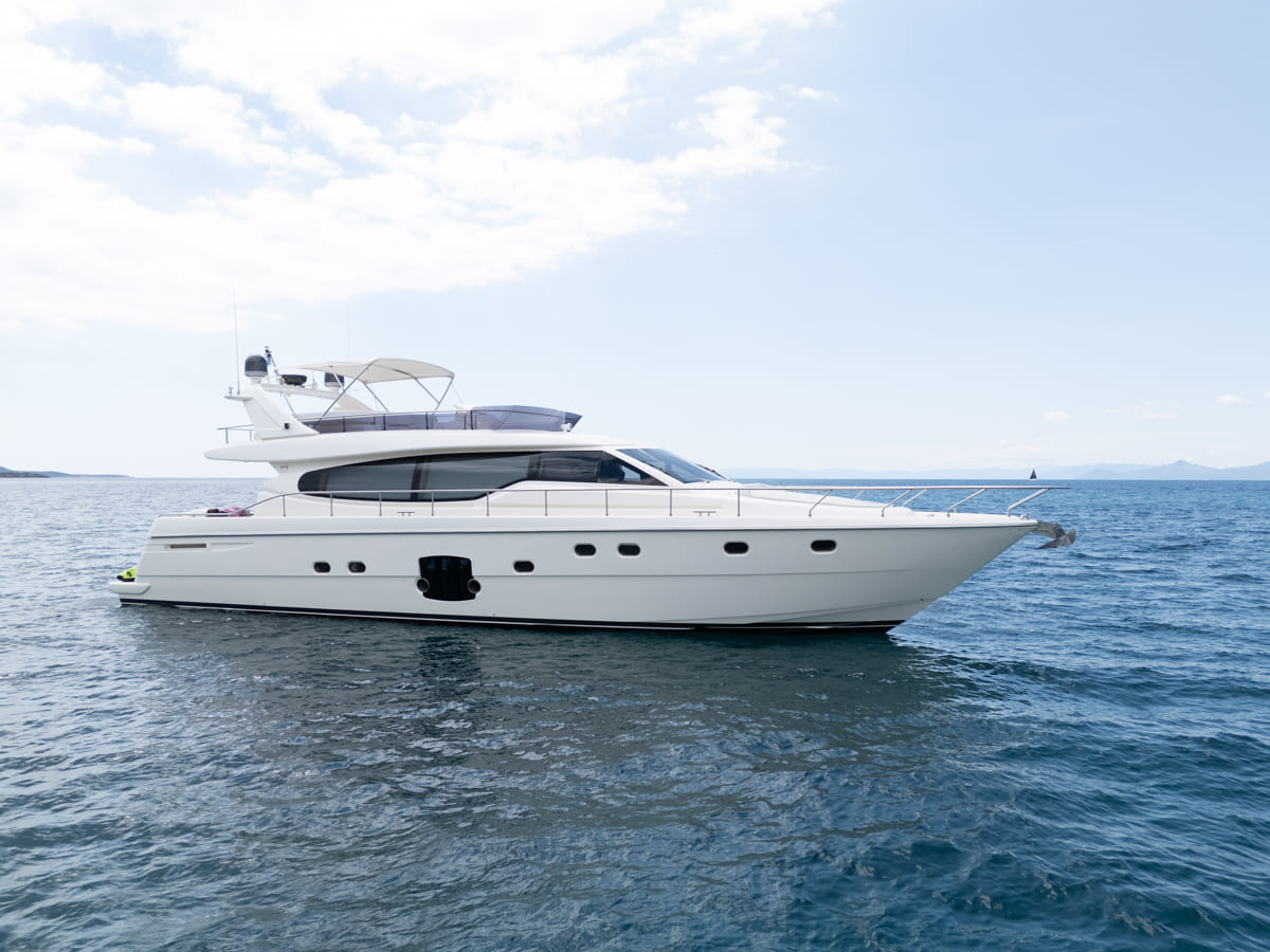 White Ferretti 63 luxury motor yacht anchored in calm blue waters with flybridge and sun awning under cloudy skies.