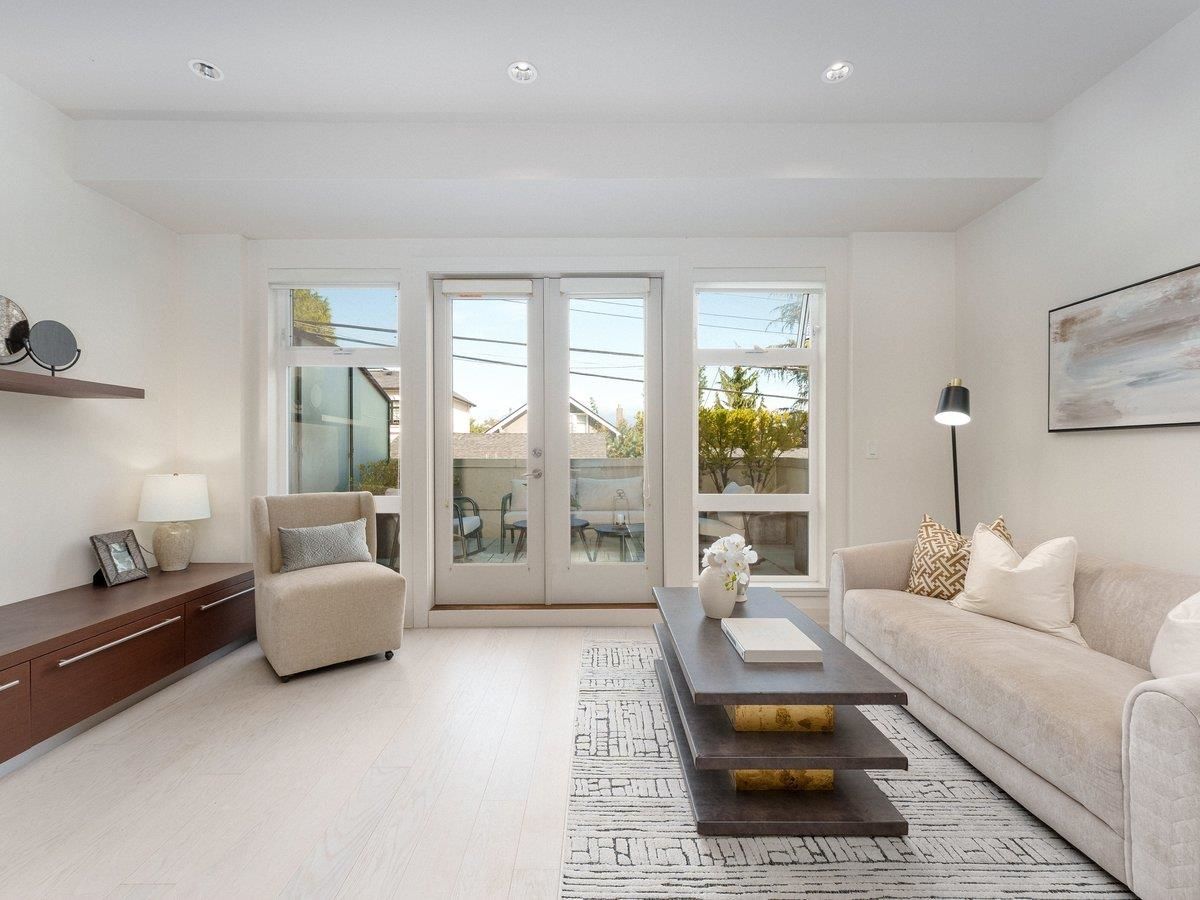 Bright living room with light walls, white furniture, and large windows, creating an open, airy atmosphere.