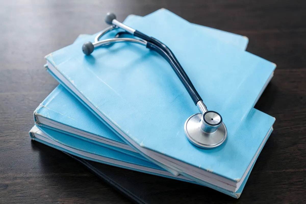 A stack of medical journals and a stethoscope arranged on a wooden desk, signifying knowledge and patient care.
