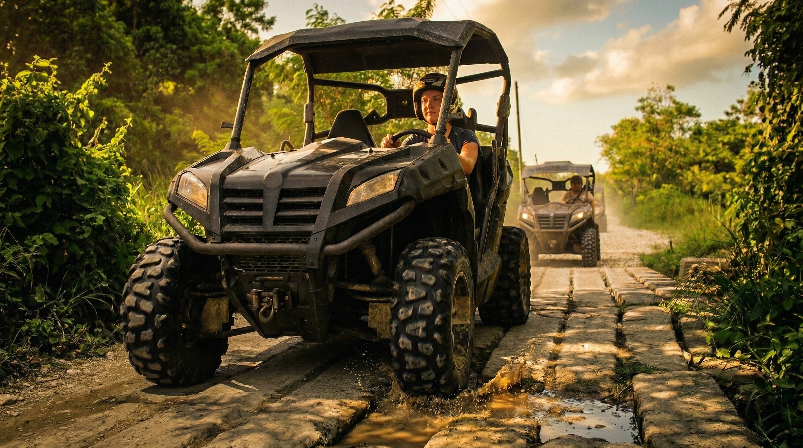 People driving black off-road buggies splashing mud on a jungle trail.