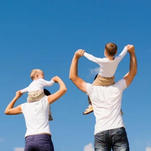 Two fathers carrying their happy young sons on their shoulders outdoors, representing healthy post-procedure recovery in Melbourne.