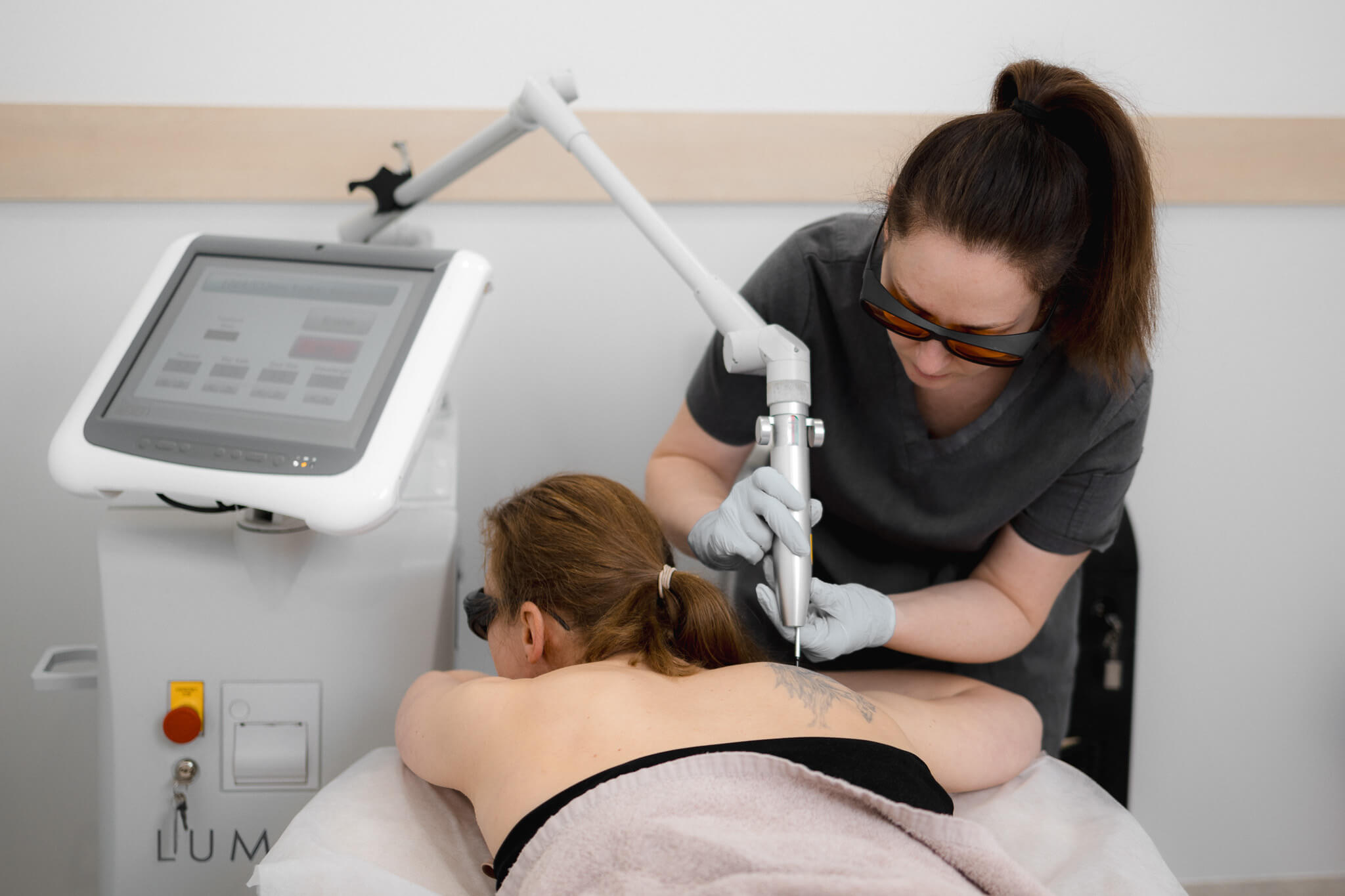 Aesthetic practitioner performing laser tattoo removal on client using medical device.