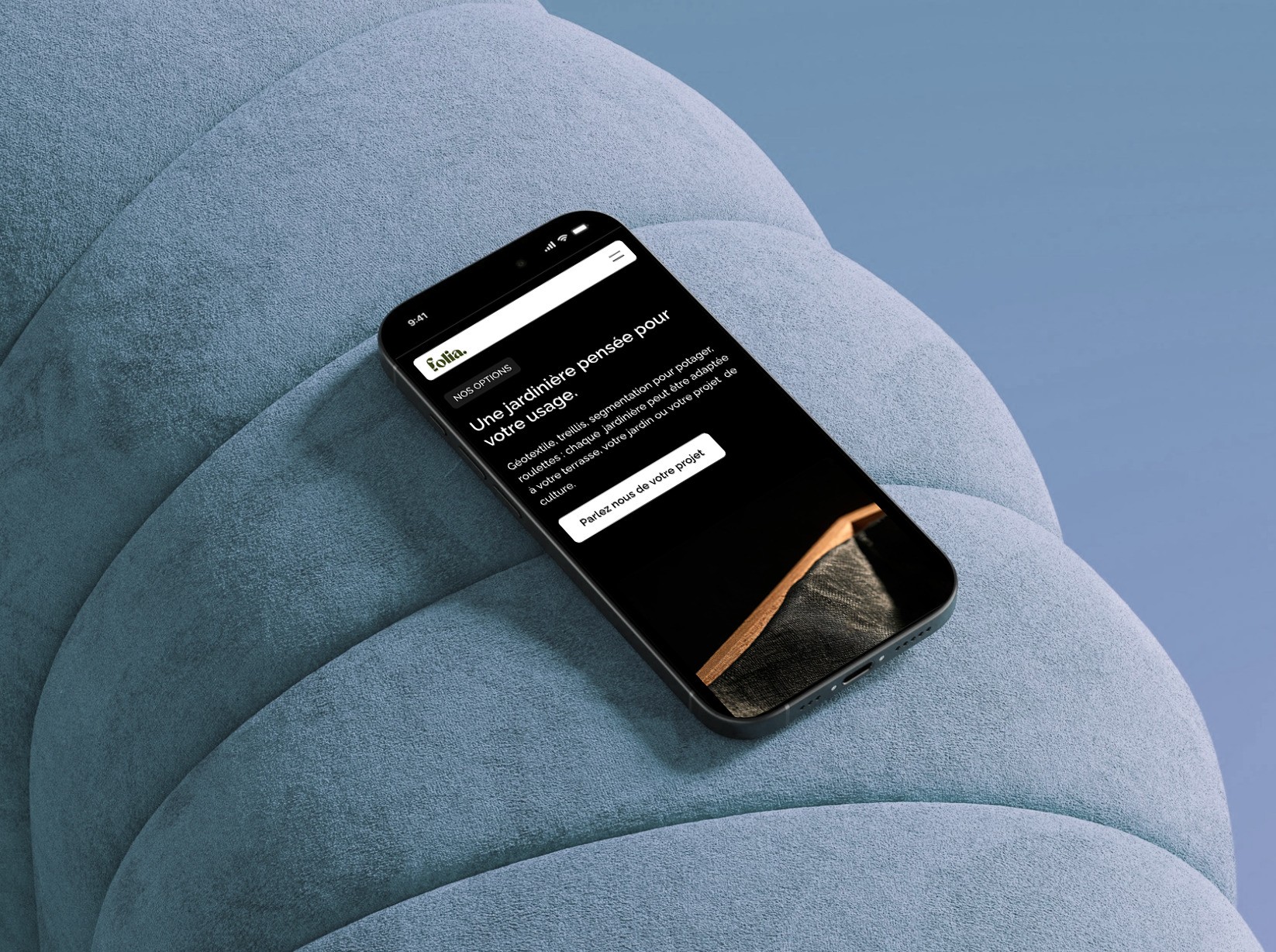 Site Folia consulté sur iPhone posé sur un pouf en velours bleu, avec le bouton Parlez-nous de votre projet