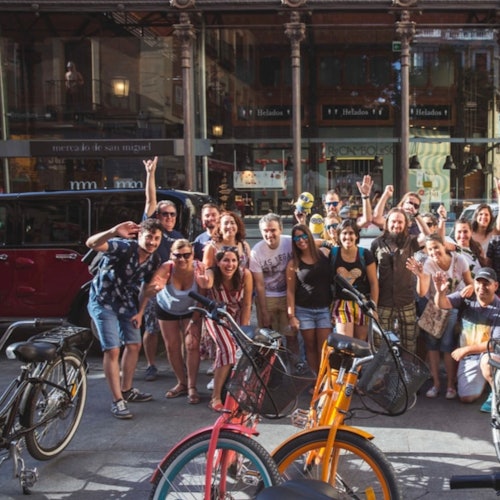 Bir mağaza önünde poz veren ve gülümseyen bir grup insan, ön planda bisikletler ve kırmızı bir araba ile.