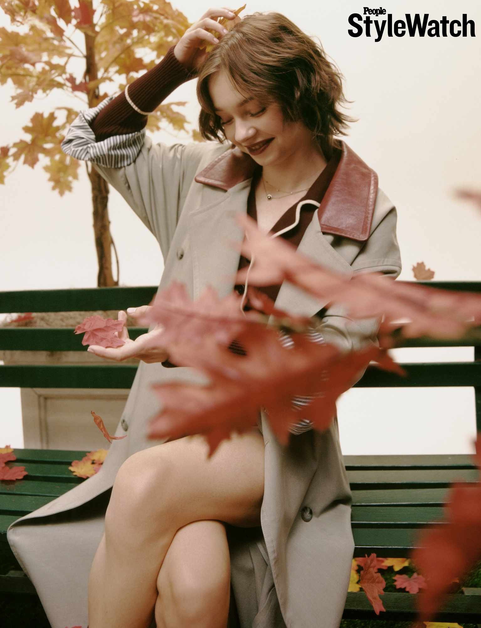 Emma Myers seated on a park bench amid autumn leaves