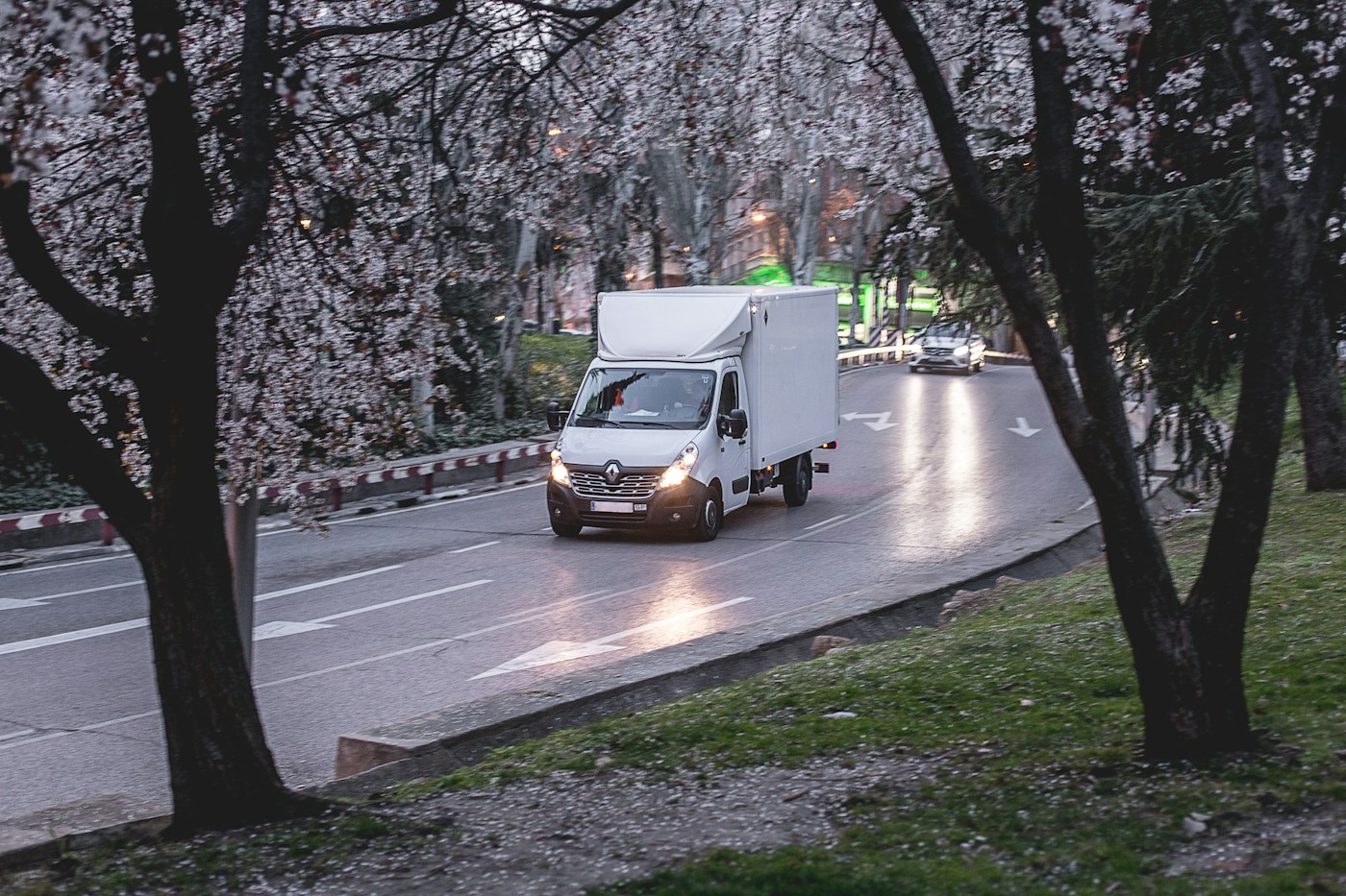 A white box van driving along a tree-lined road