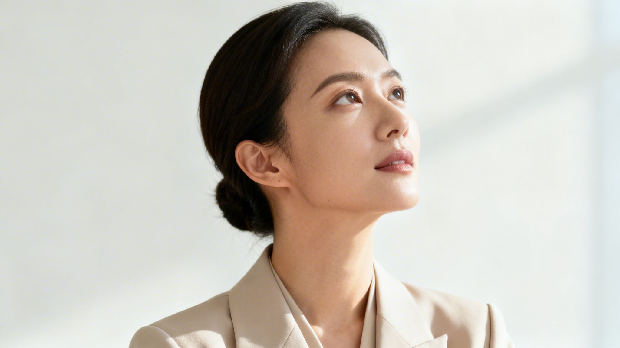 Porträt einer eleganten Frau im beigen Blazer, die mit erhobenem Blick ins sanfte Licht schaut.