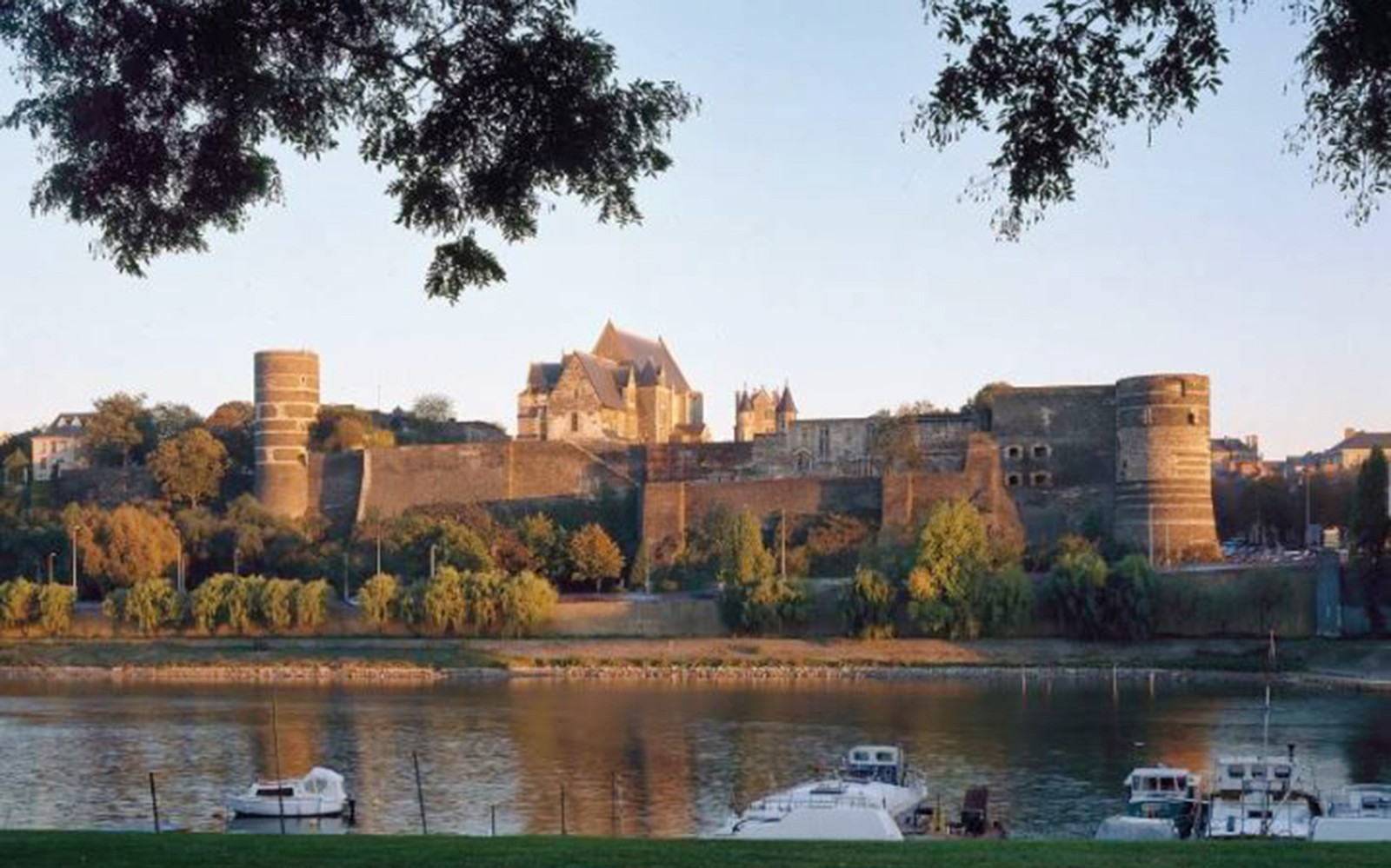 Panoramic view of Angers Castle with river and boats in foreground, France.