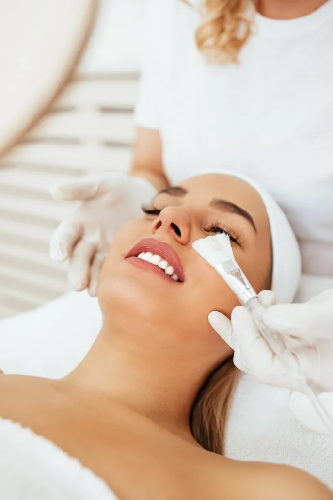 Aesthetician applying facial mask during rejuvenating facial to purify skin, eliminate bacteria, and promote healing.