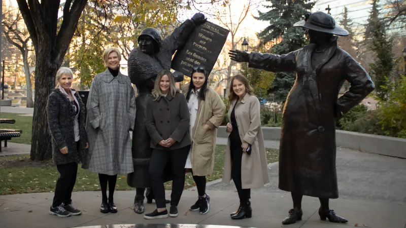Image of Women in coats standing beside statues in a park, symbolizing empowerment and equality in KHD Homes community.