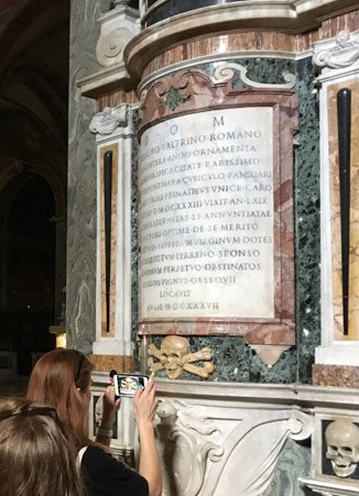A photo of a man taking a picture with is phone of an engraved text on a round wall.