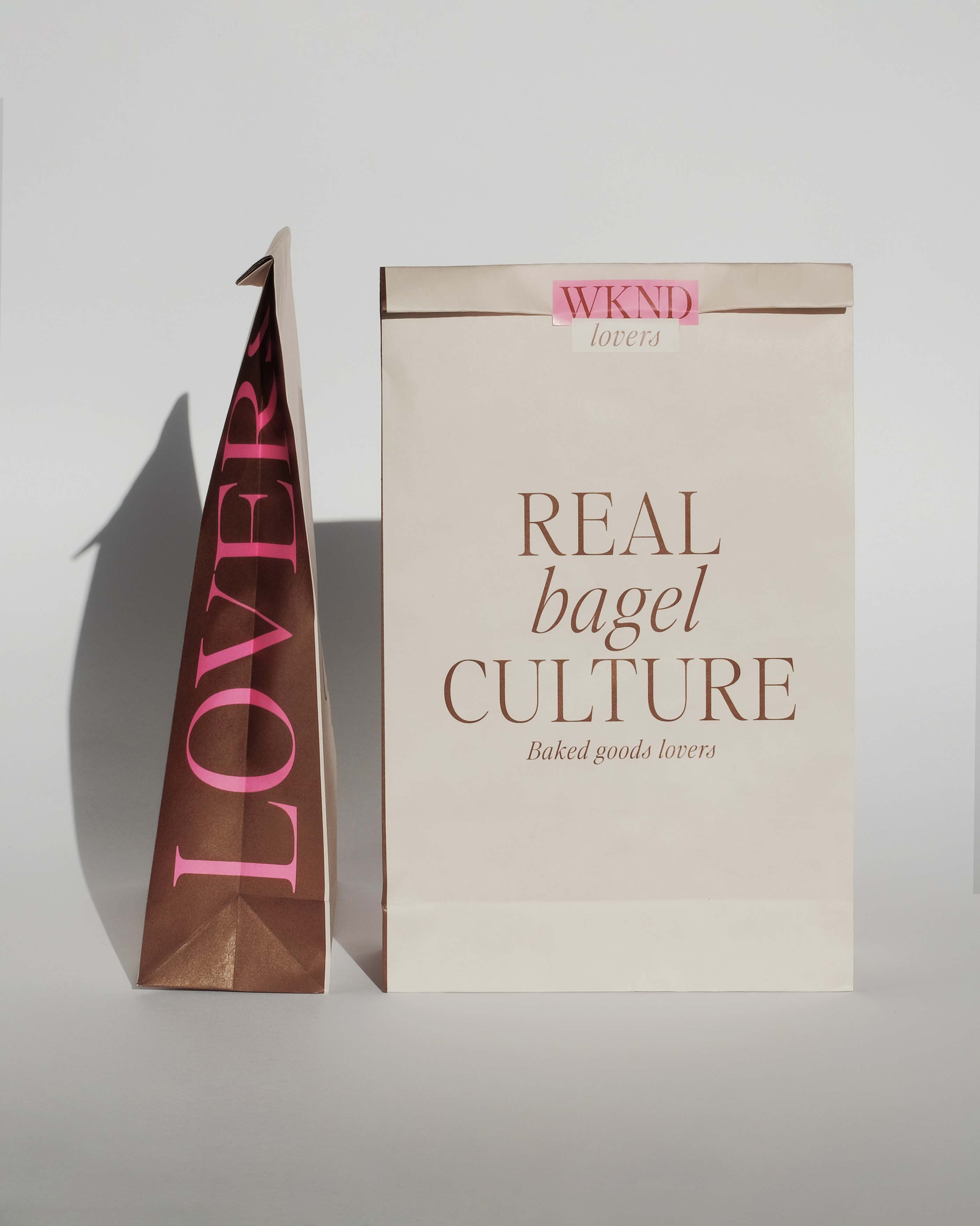 Two paper bags with the words "Real Bagel Culture" and "Lover" on them. It says "WKND" at the top of one bag.