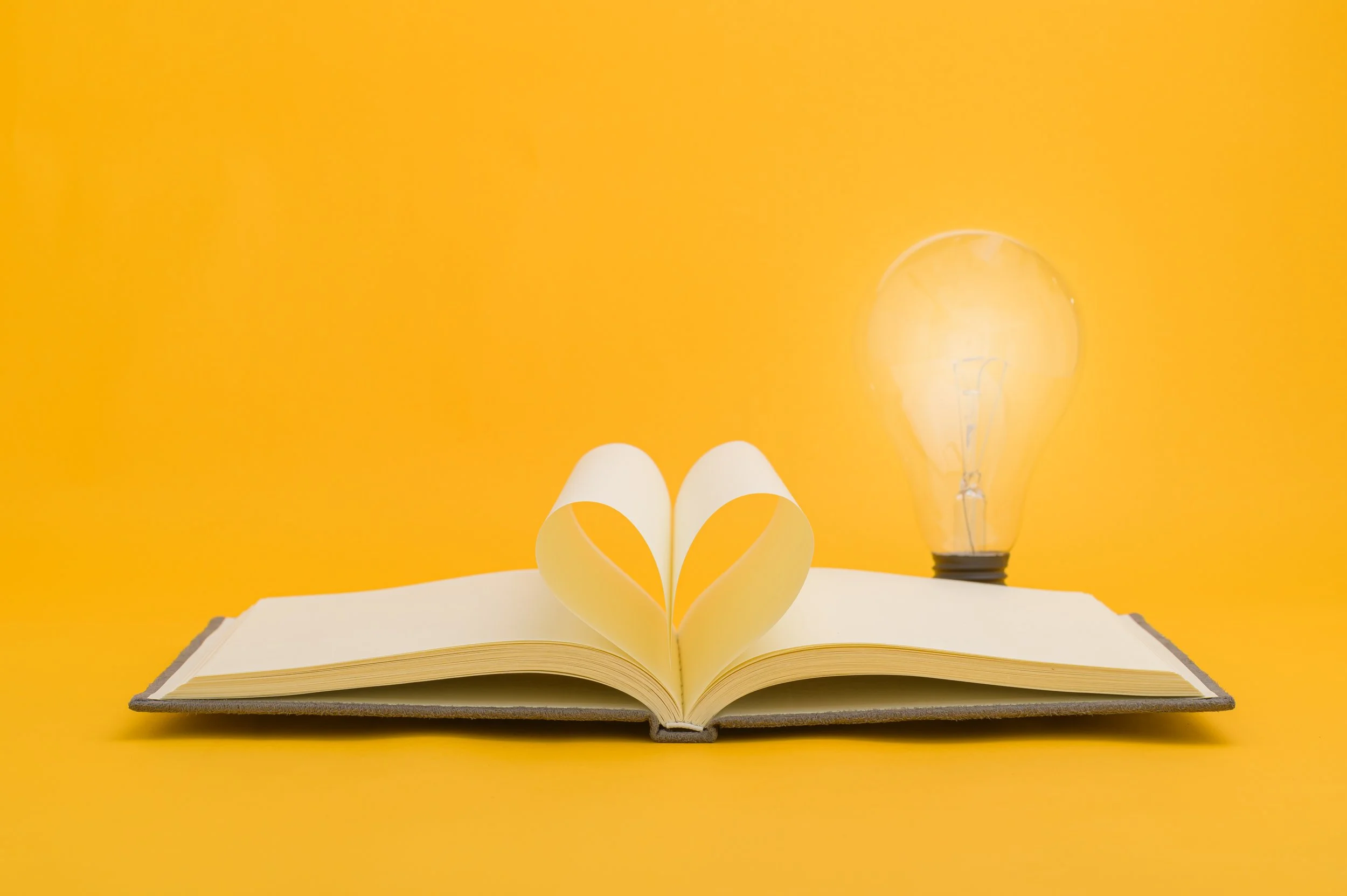 Book with papers making a heart shape with light bulb