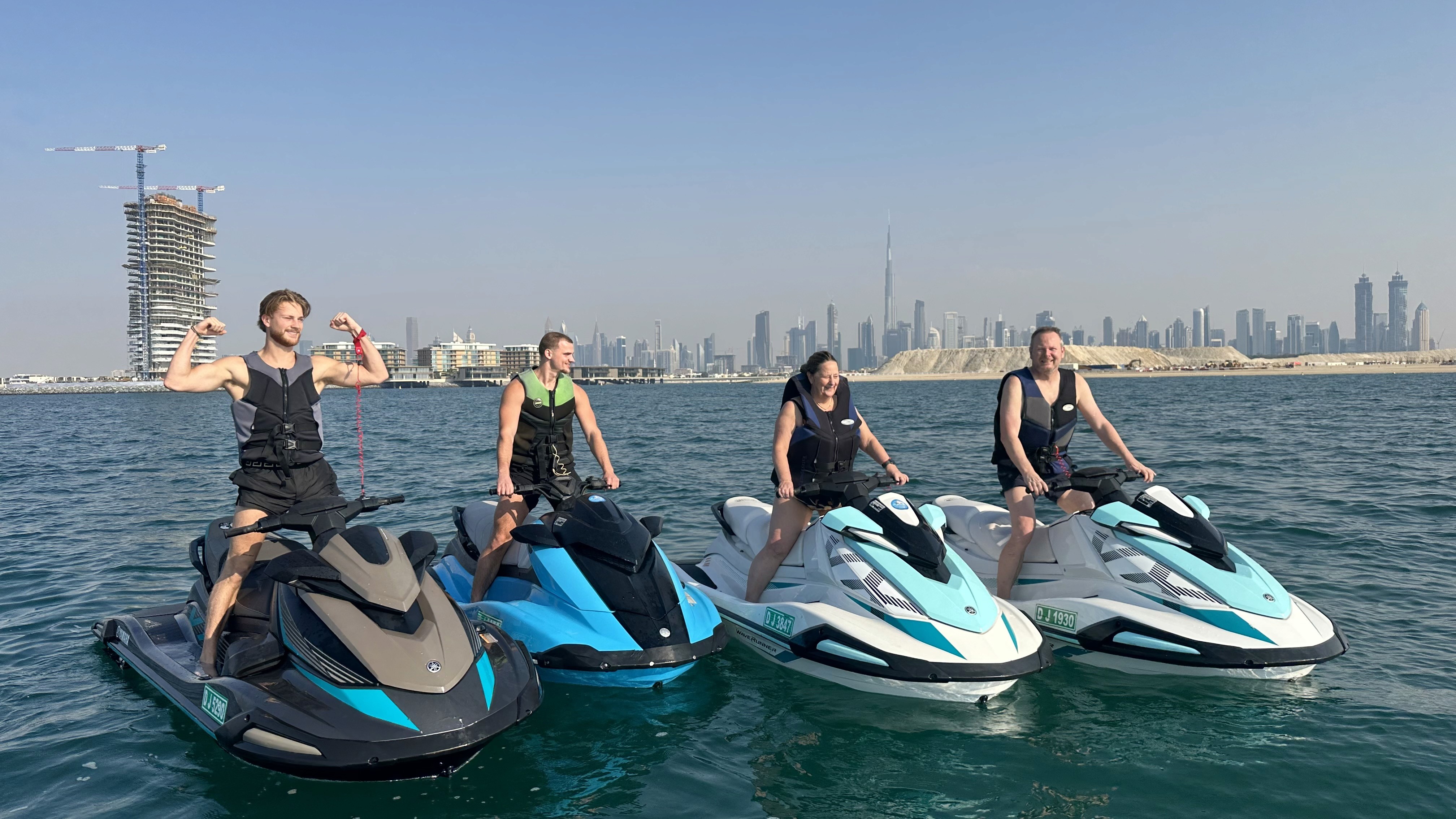 A group of four friends posing on their jet skis in the ocean with the Dubai skyline and Burj Khalifa in the background.