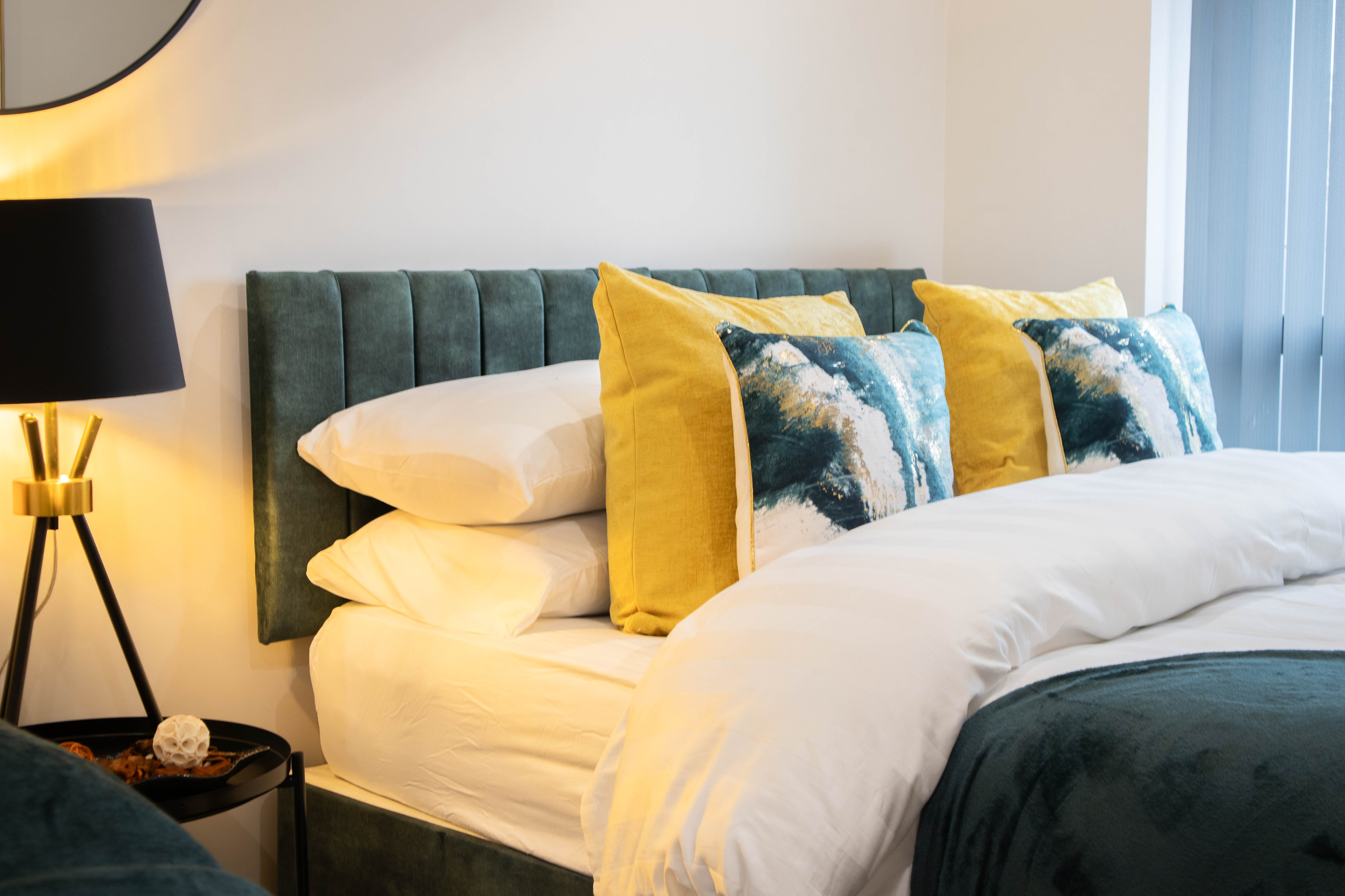 Bright Airbnb double bed with green throw and yellow cushions