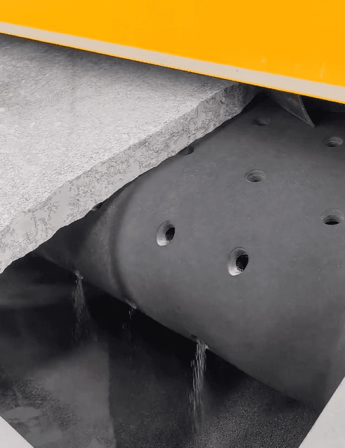 The polishing process of a granite slab as it passes through an industrial roller under a polishing machine.