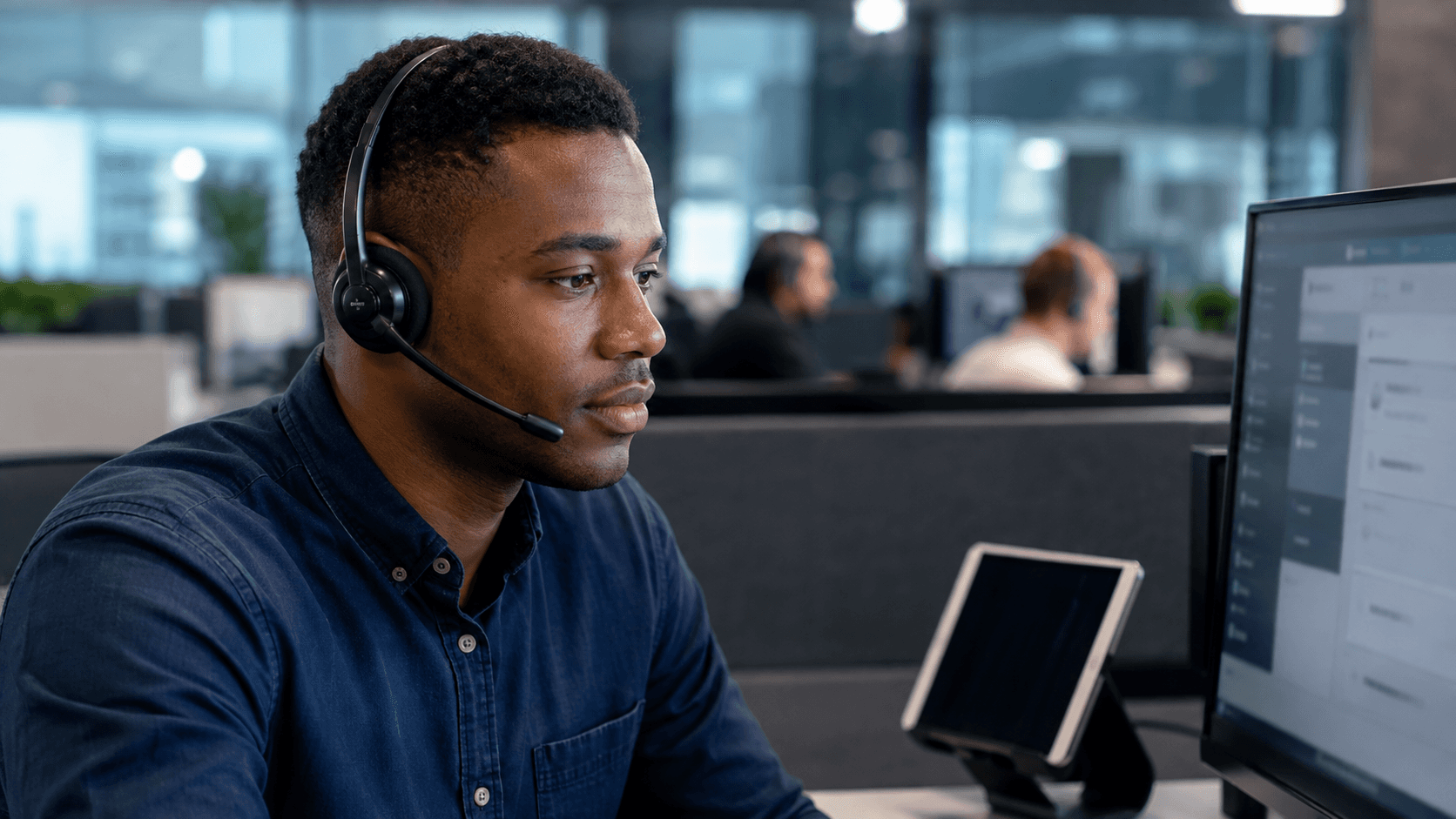 A technical-support advisor wearing a headset assists customers from a modern contact-centre workstation.