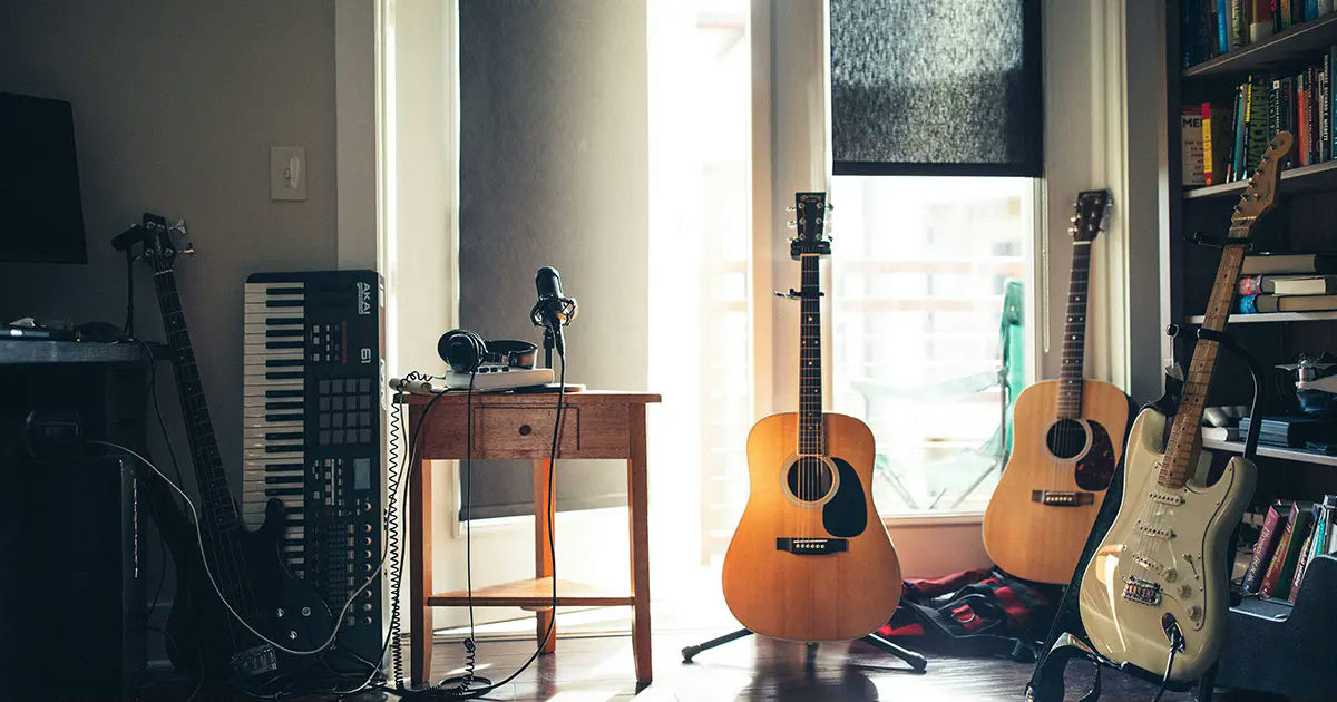 Home music studio with guitars, a keyboard, and a microphone setup near a window.