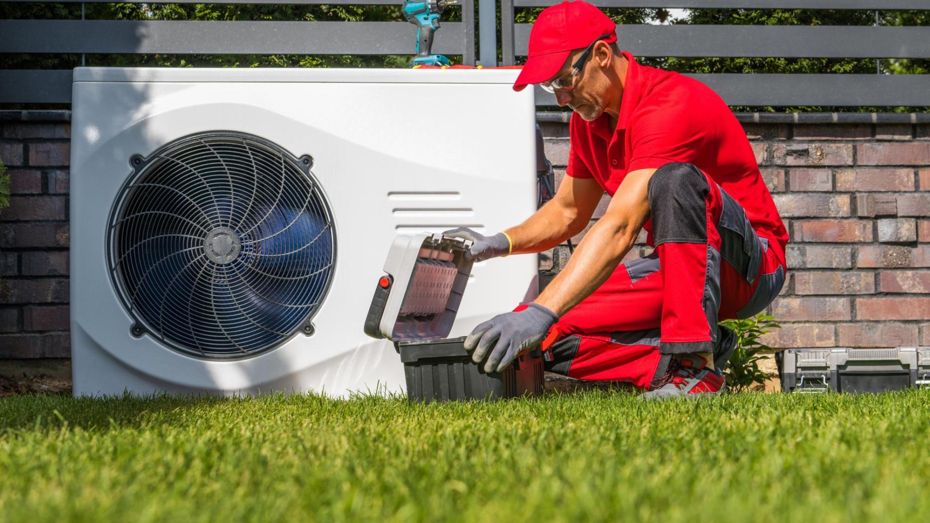 Techniker in roter Arbeitskleidung installiert eine Luft-Wasser-Wärmepumpe im Garten