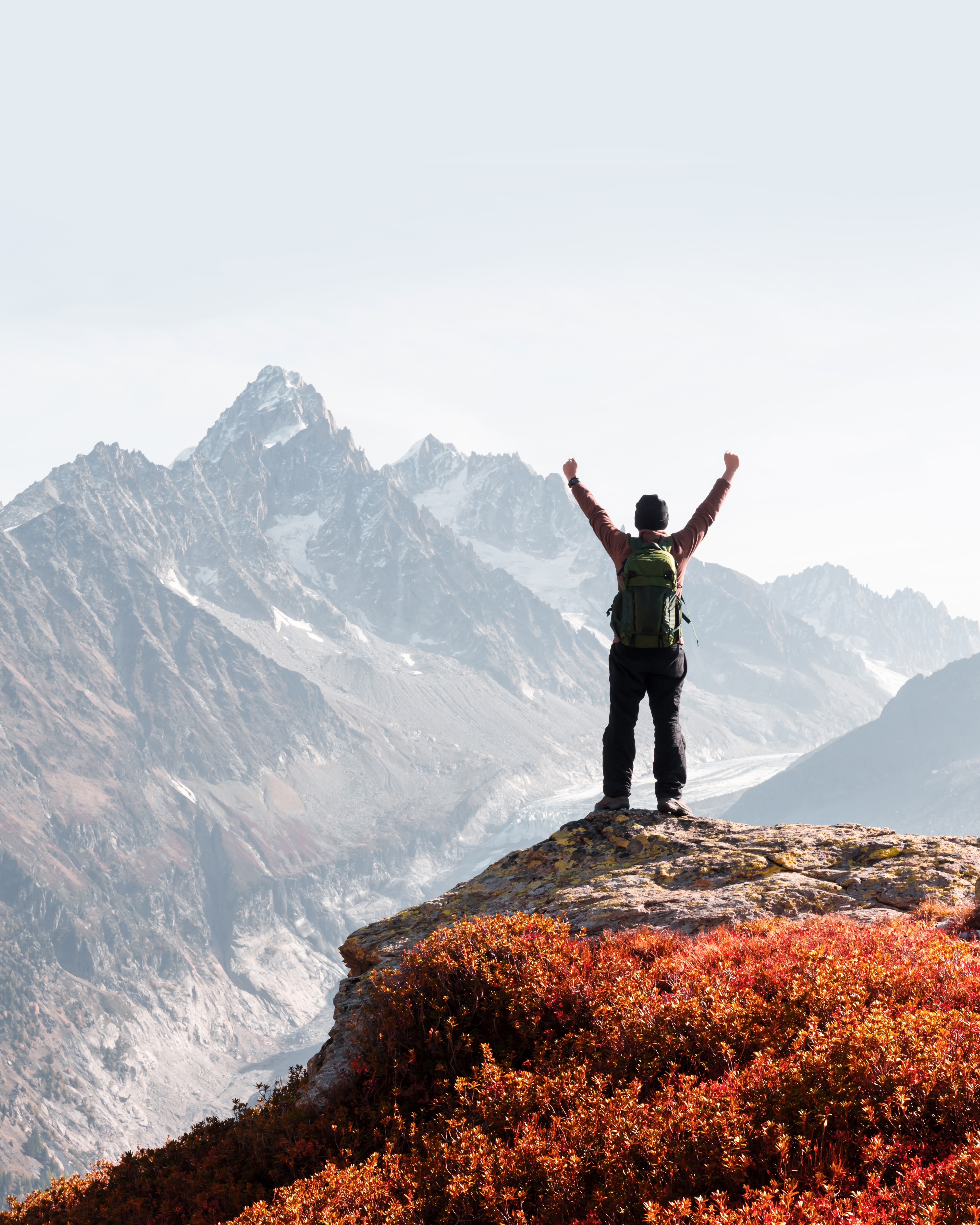 A hiker celebrates at the top of a mountain trail