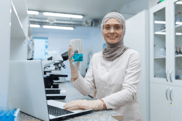 Confident woman standing in a brightly lit hospital corridor with medical monitors and equipment in the background.