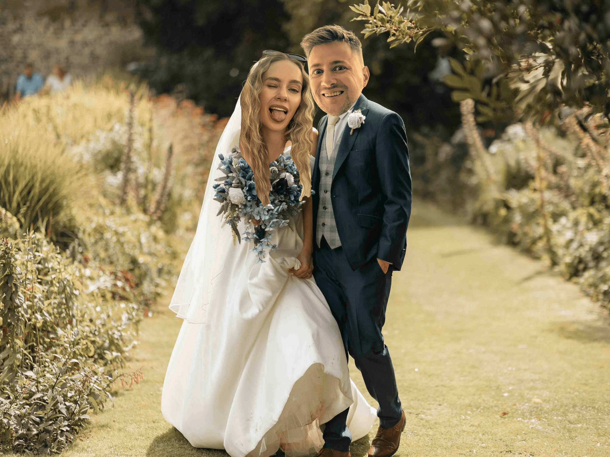 A bride and groom hold hands tenderly, the bride's bouquet of dried flowers hanging low. They stand in a softly lit, elegant interior, conveying romance.