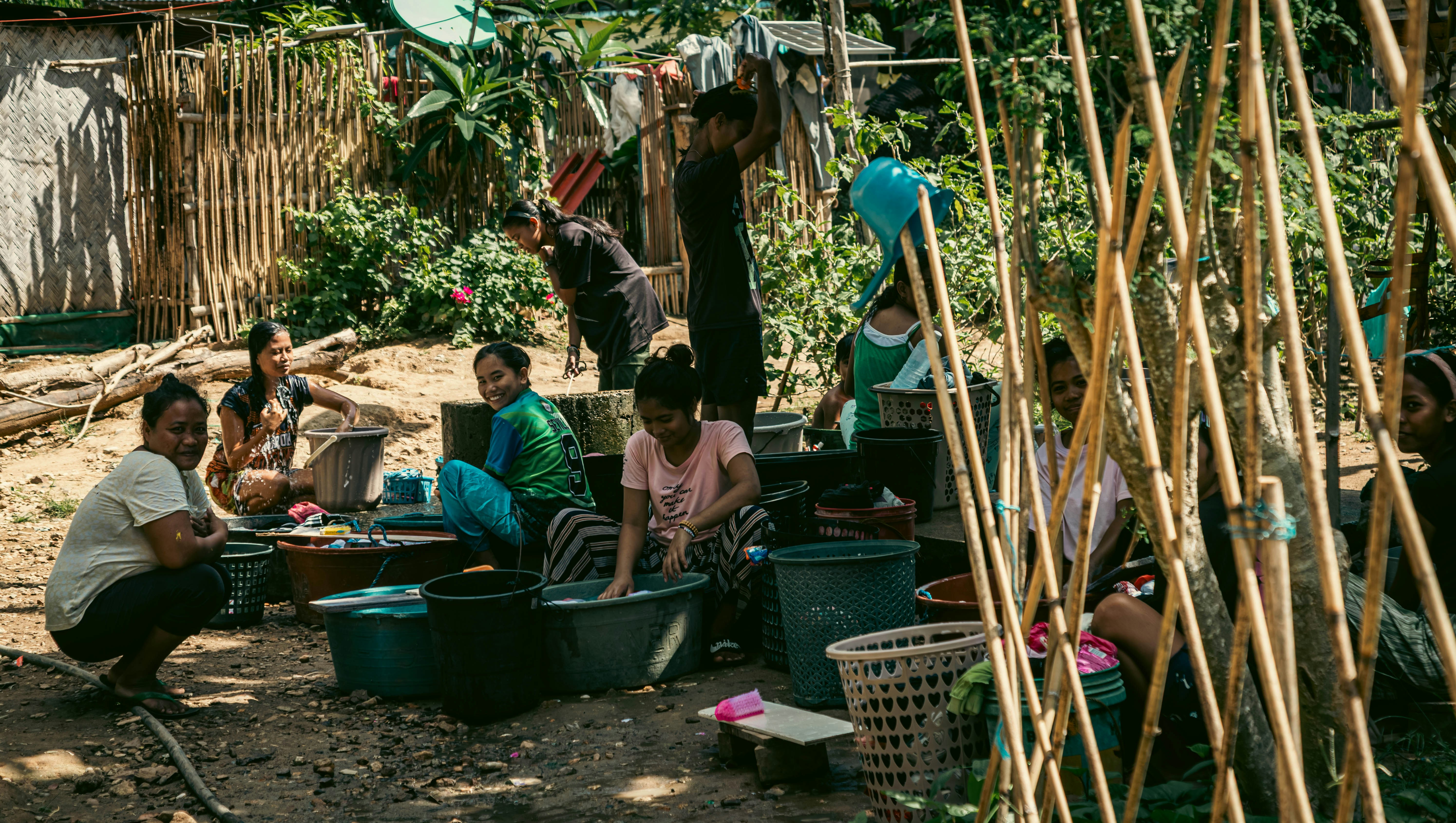 philipinische Frauen waschen Kleidung in Wasserbecken im Freien und lächeln in die Kamera