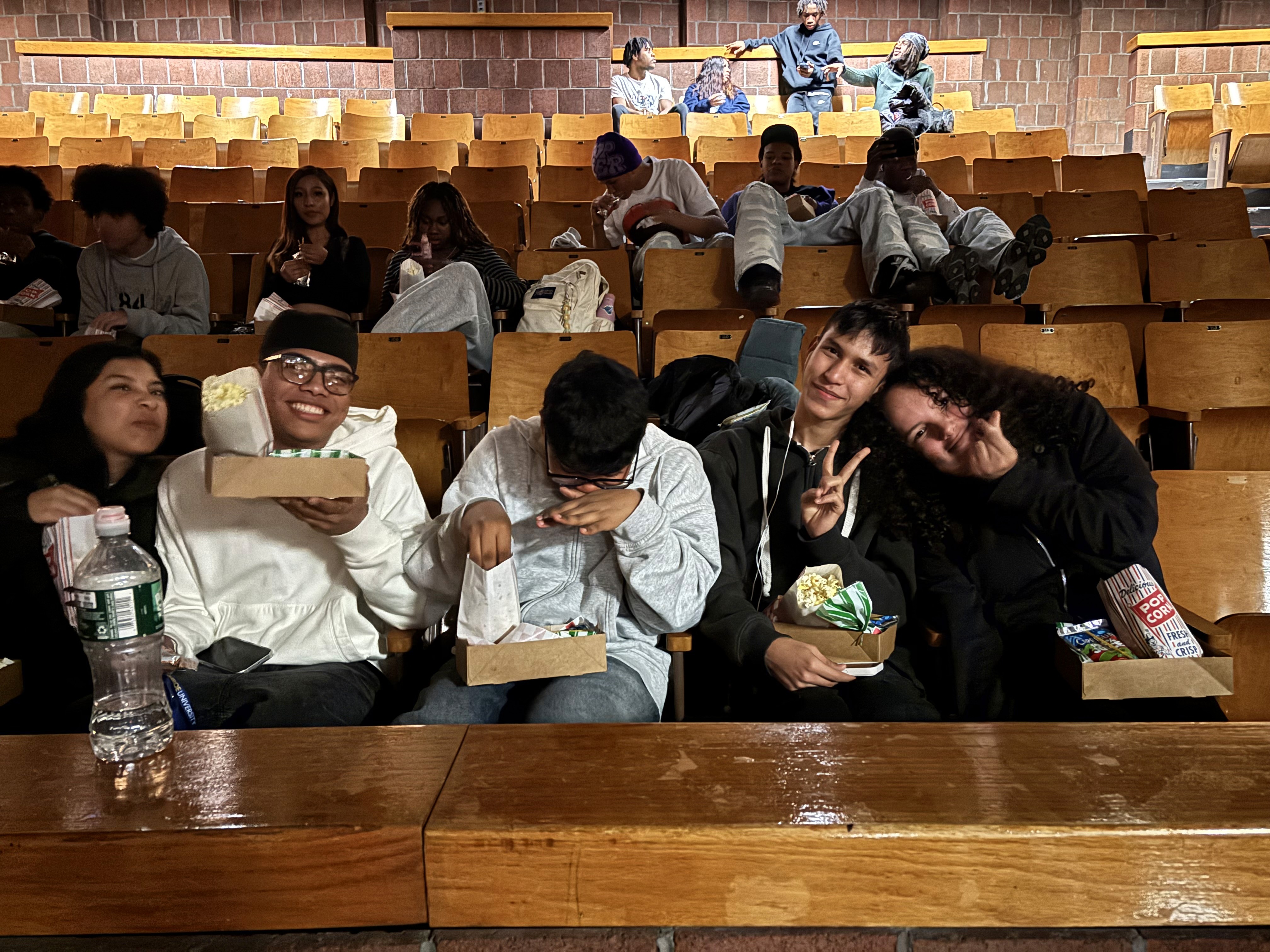 Youth participants gather in a school auditorium with snacks to watch a movie.