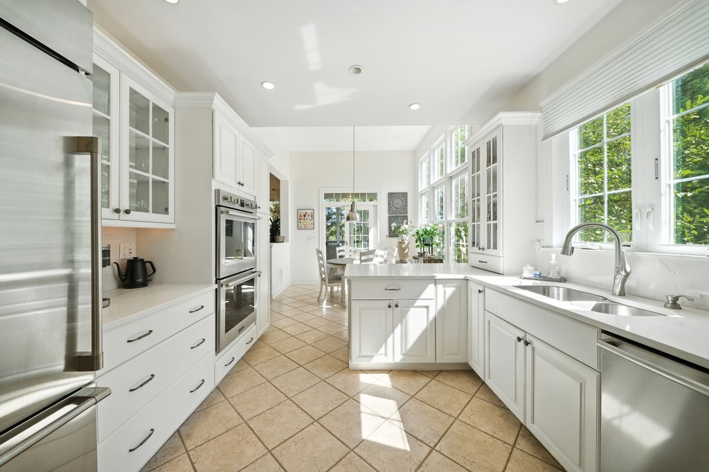 A modern hallway features vibrant teal and orange geometric and leaf patterns, with glossy tiled floors, a large rectangular light fixture, and a small shelf holding a potted plant, all leading to a large, frosted window at the end.