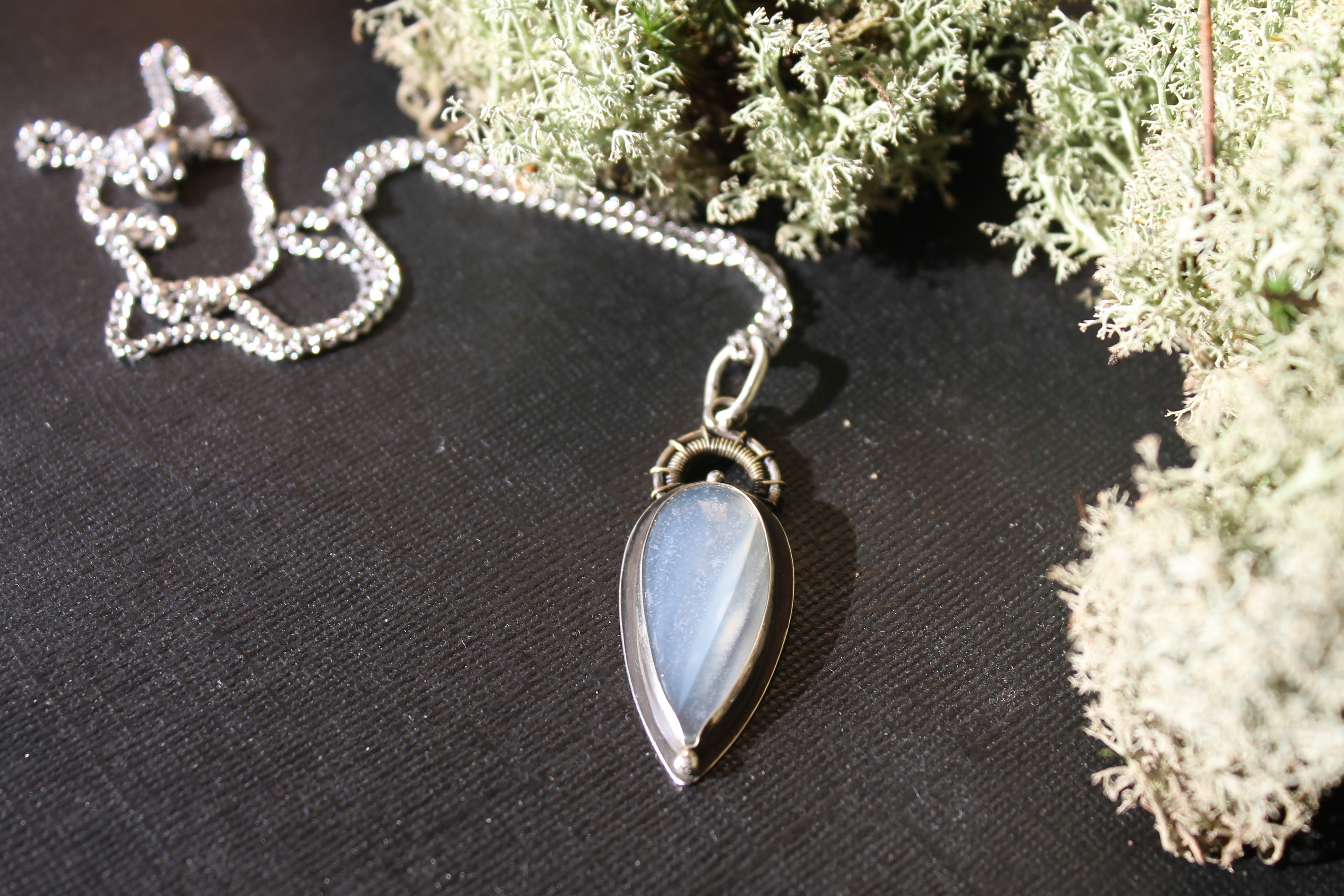 Silver necklace with a teardrop pendant on dark surface
