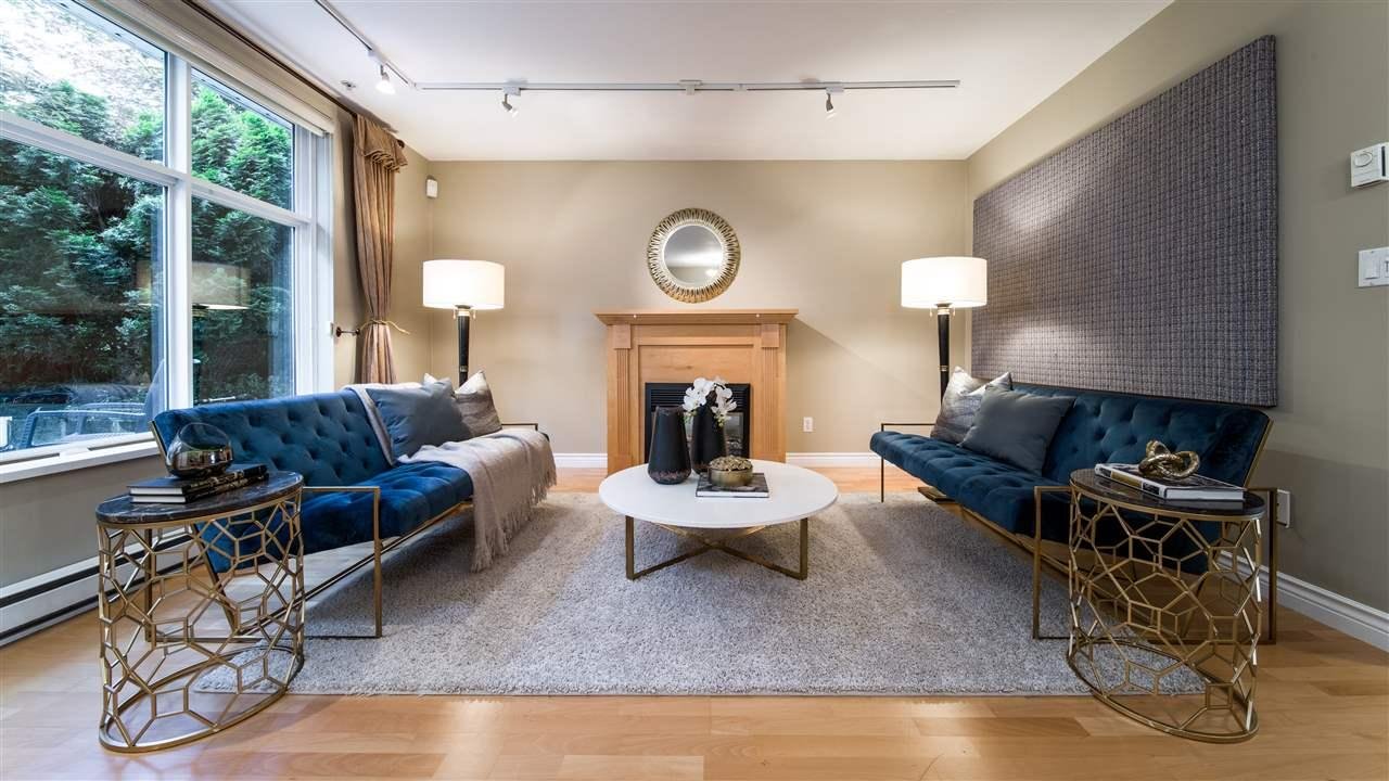 A modern living room featuring blue sofas, a coffee table, and a cozy fireplace with large windows letting in natural light.