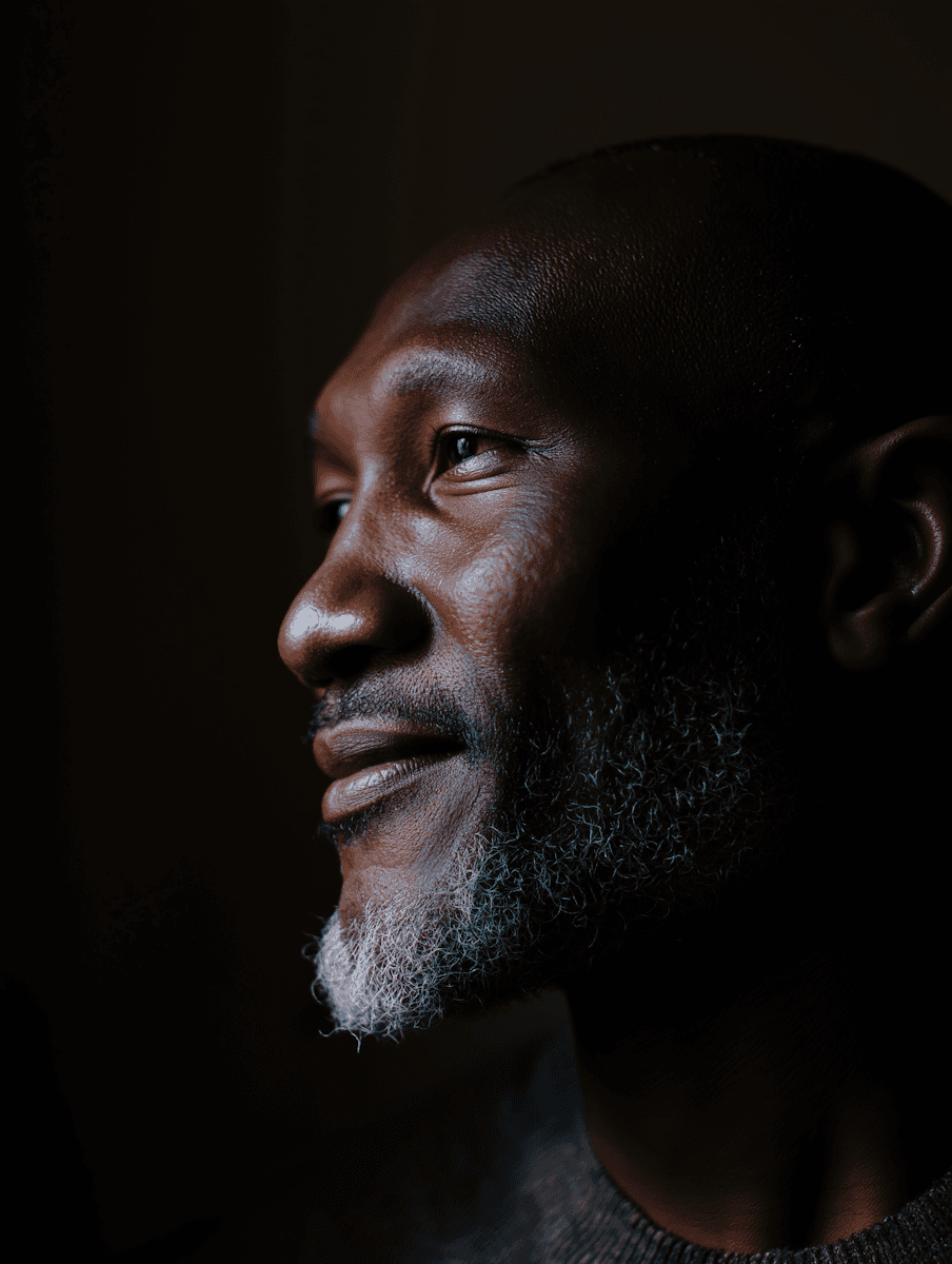 A dramatic side-profile portrait of a handsome older man with a dark background, emphasizing his contemplative expression and white beard.