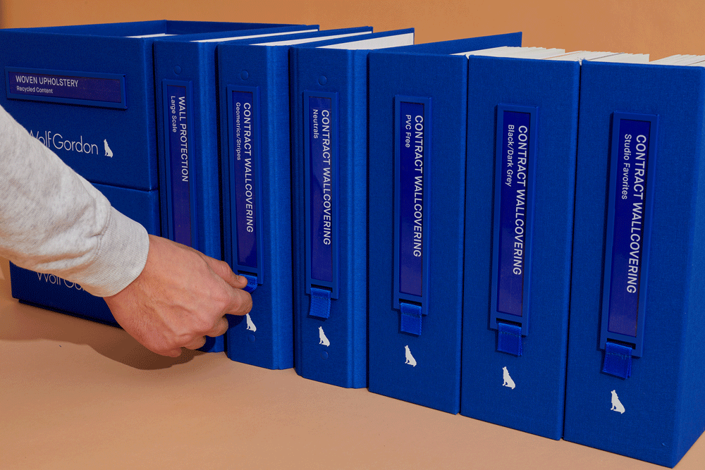Hand pulling a blue Wolf-Gordon material sample binder from a row of binders