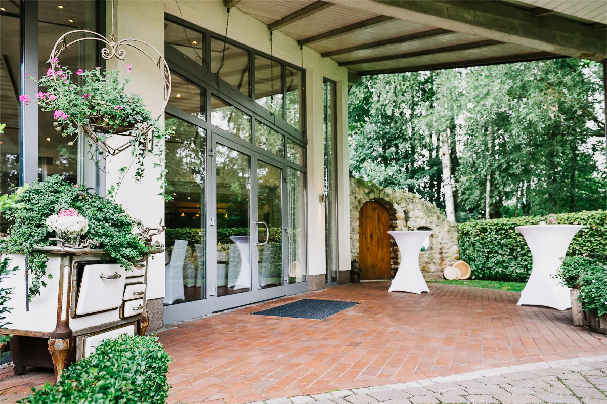 Außenansicht eines Restaurants mit Glasfront, weißem Geschirr und Blumenarrangements vor der Tür.