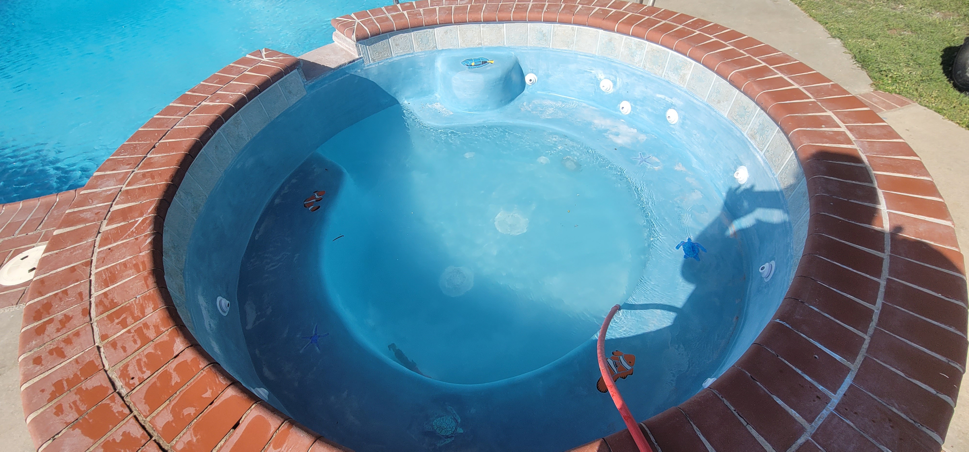 Top view of an outdoor circular Jacuzzi with red brick finishes and a blue interior lining.