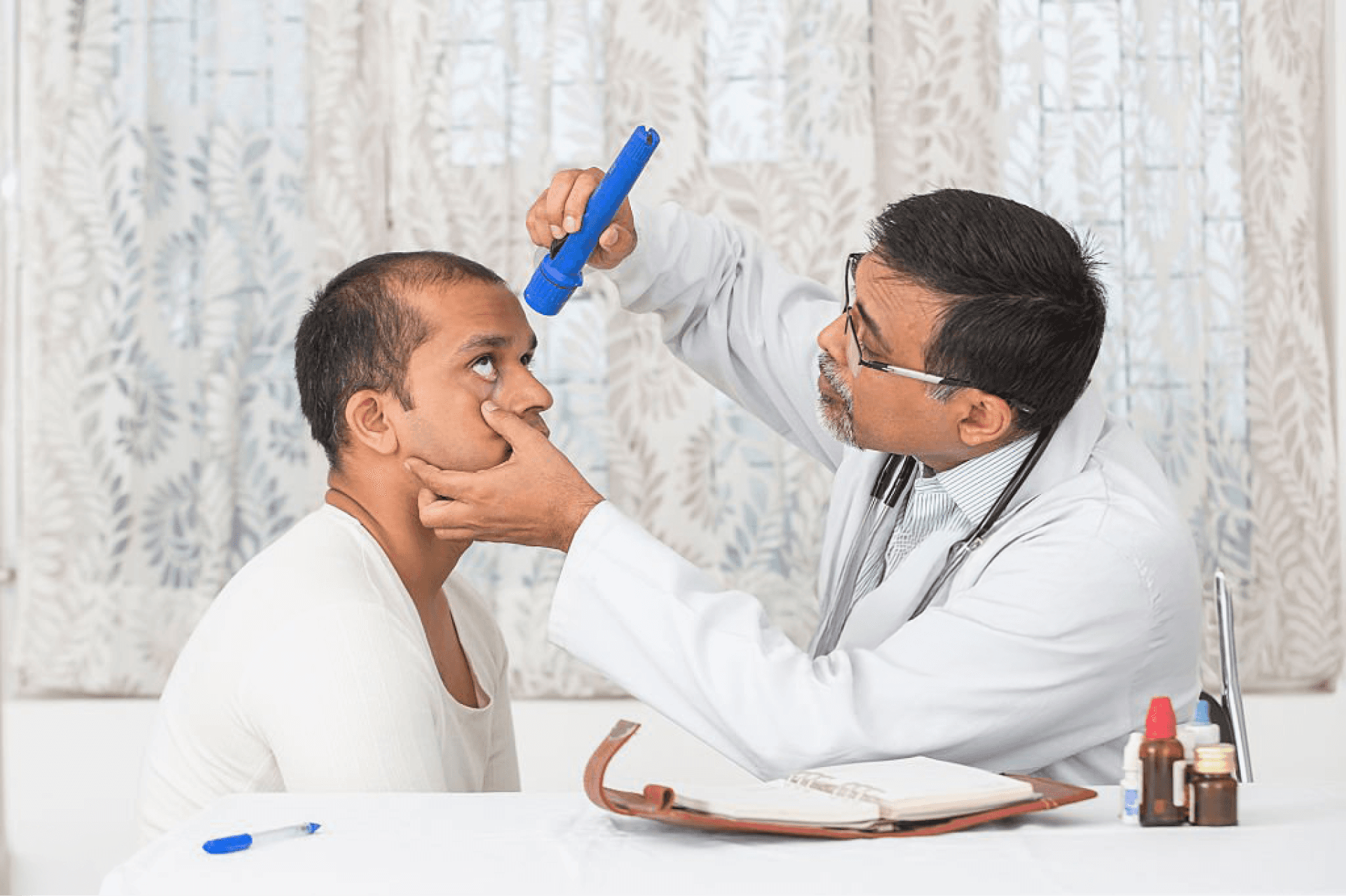 An Indian doctor examining a patient’s eyes with a flashlight during a medical check-up.