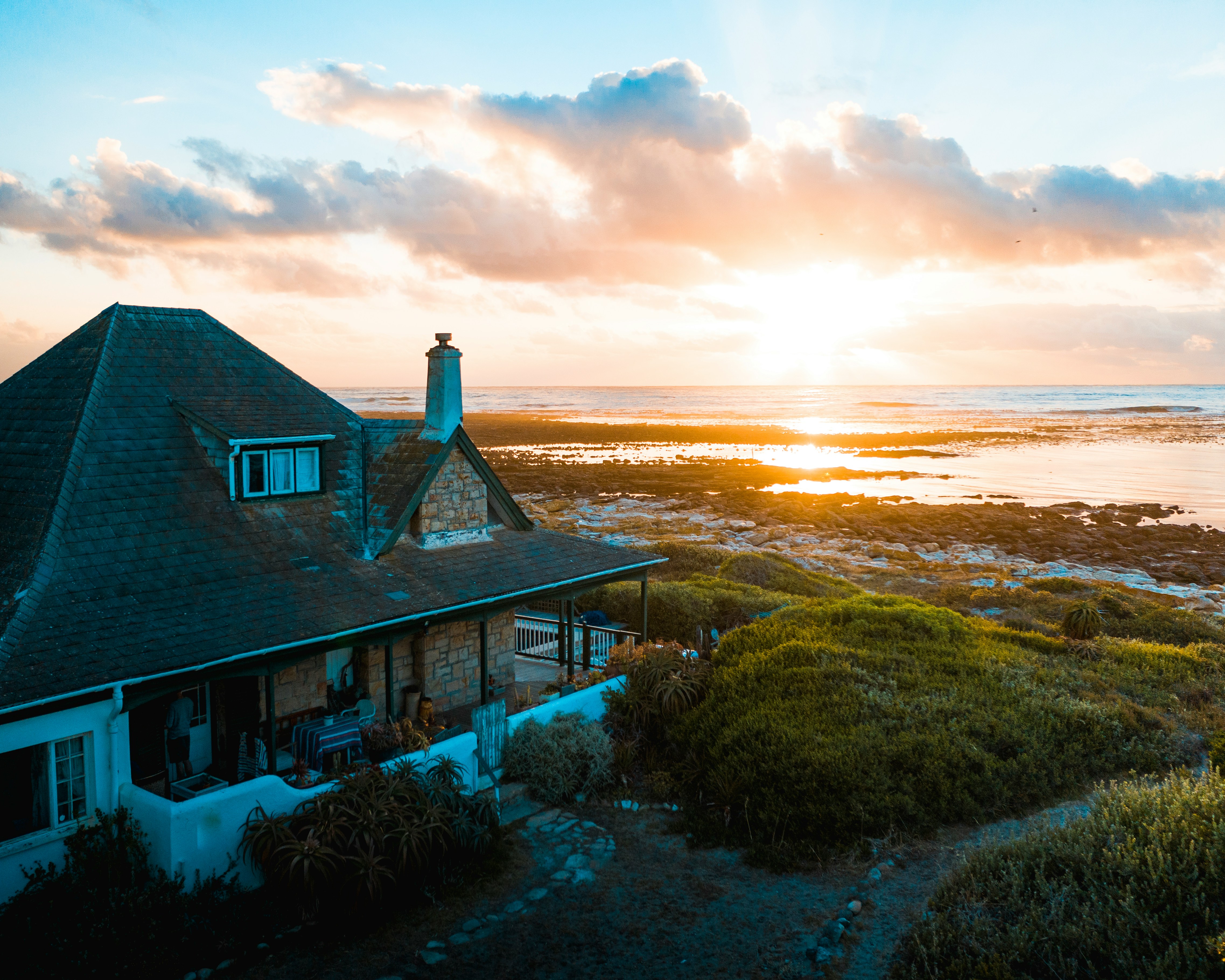 Rustic cottage with a thatched roof and a dramatic sunset.