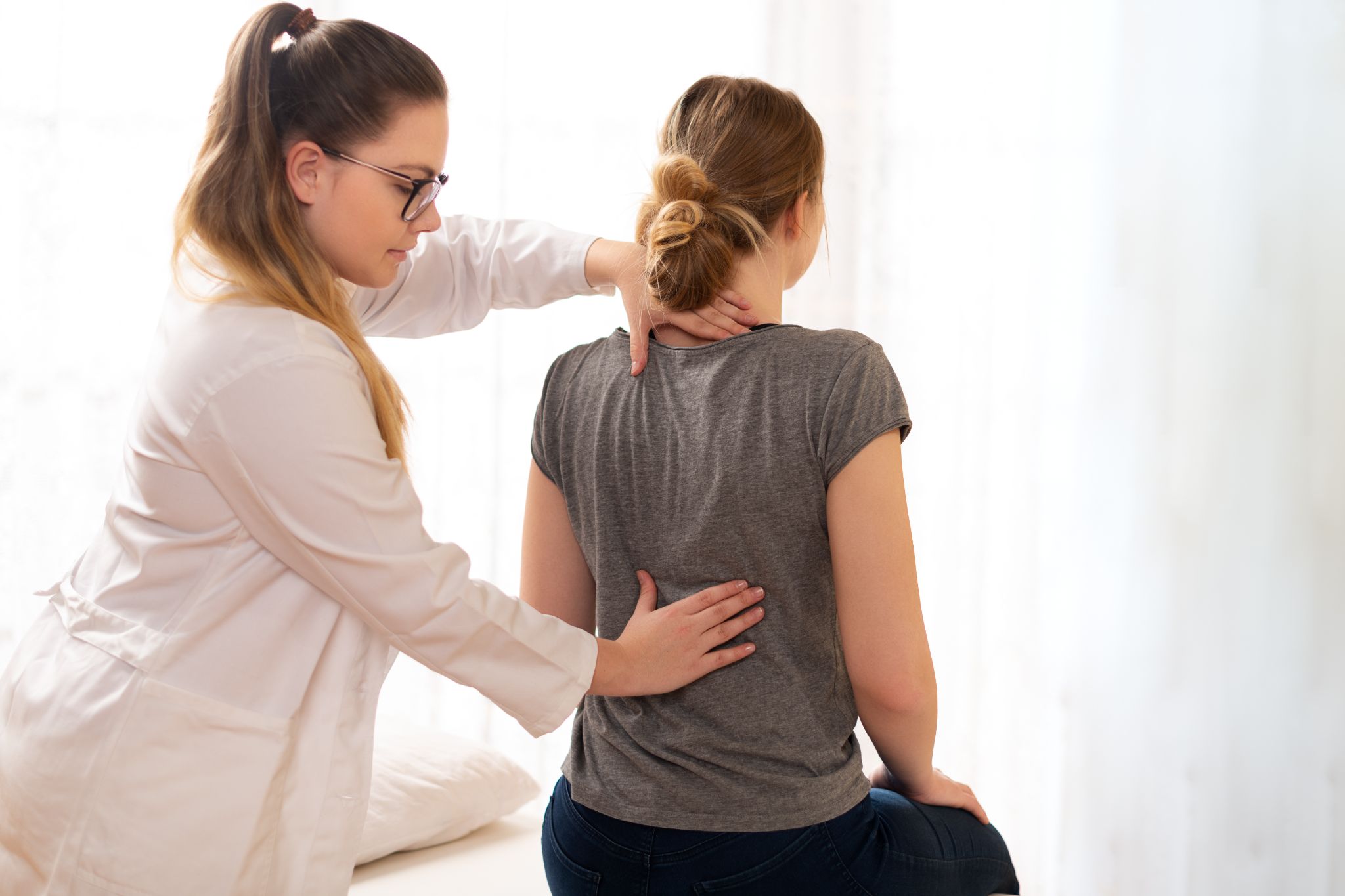 A physical therapist or doctor examining a female patient's back and neck.