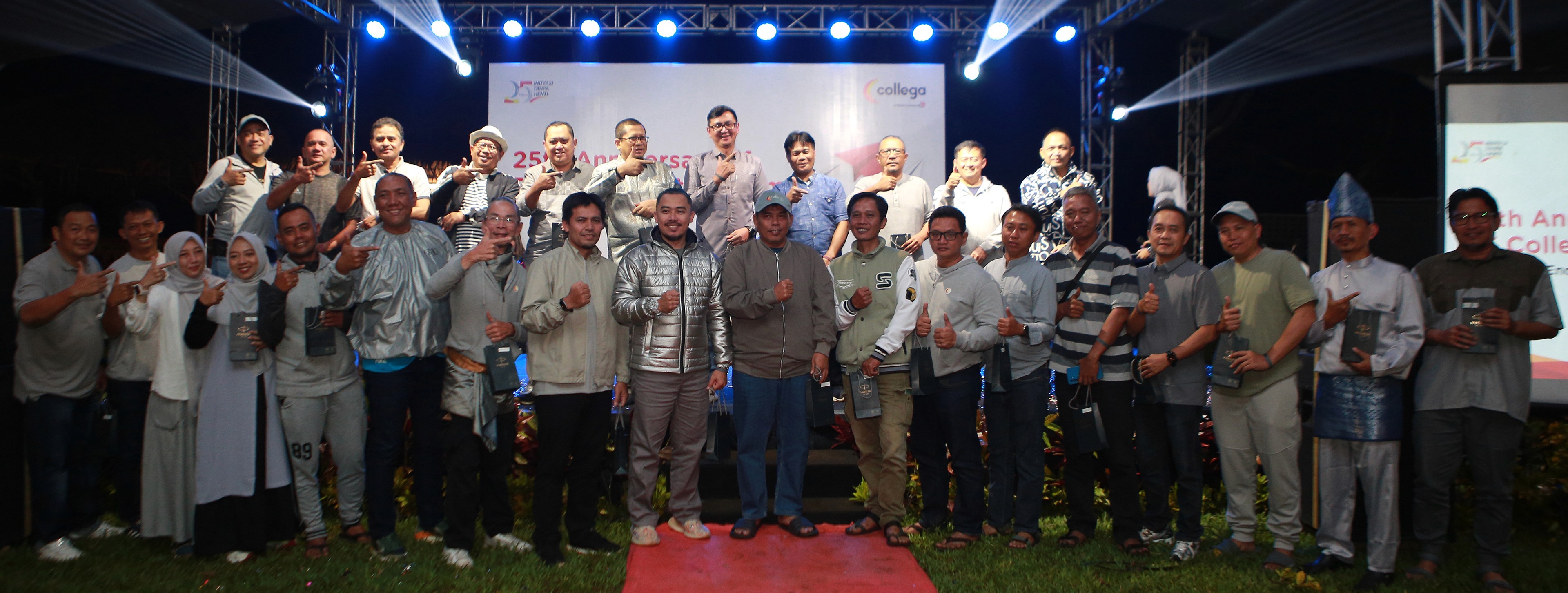 Sekelompok karyawan dan manajemen berfoto bersama di atas panggung dengan pencahayaan lampu sorot biru, latar backdrop perayaan 25th Anniversary Collega, serta karpet merah di bagian depan panggung