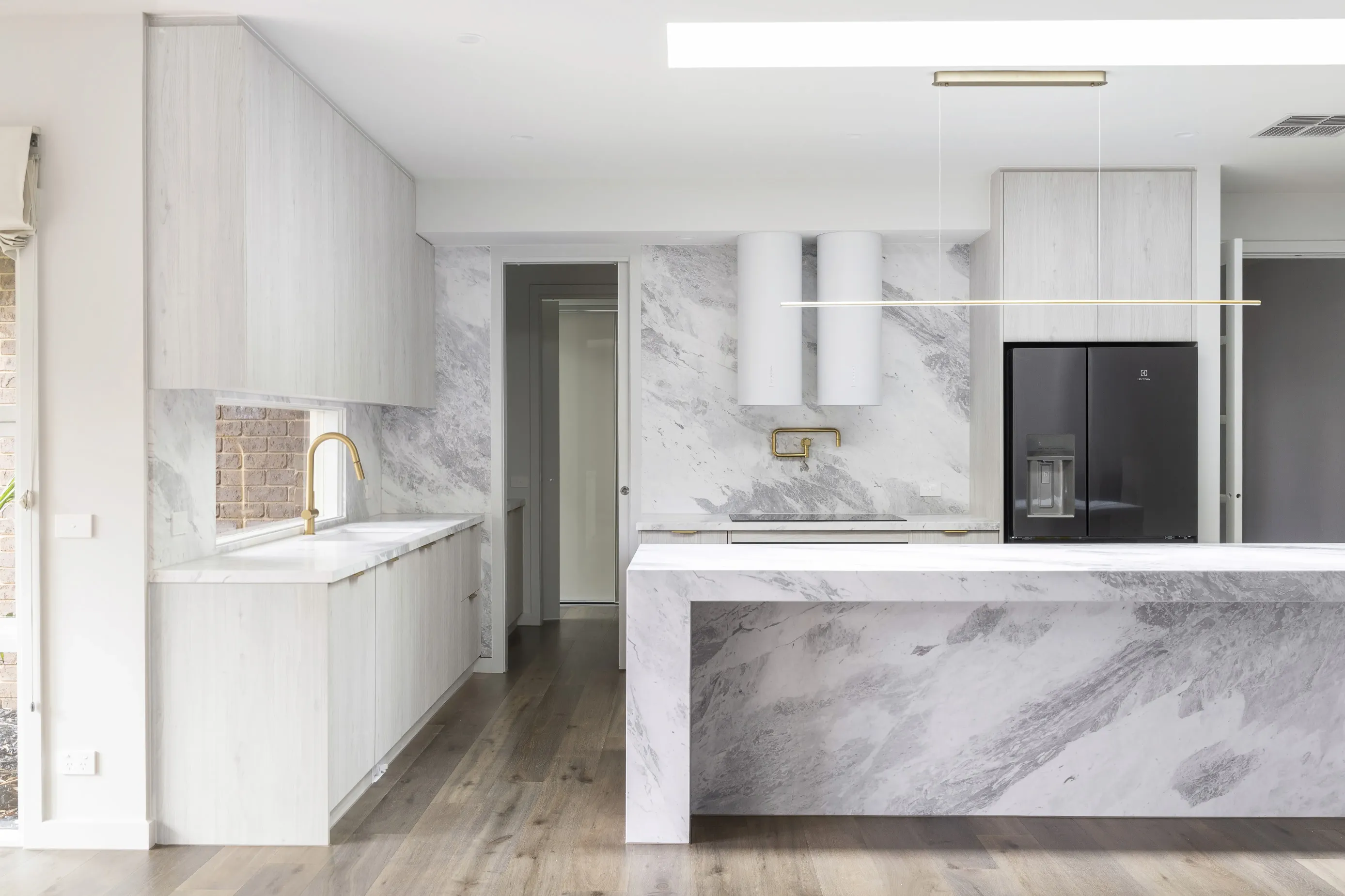 Bundoora kitchen with twin white cylinder rangehoods, dramatically veined marble splashback and a brick-framed window nook