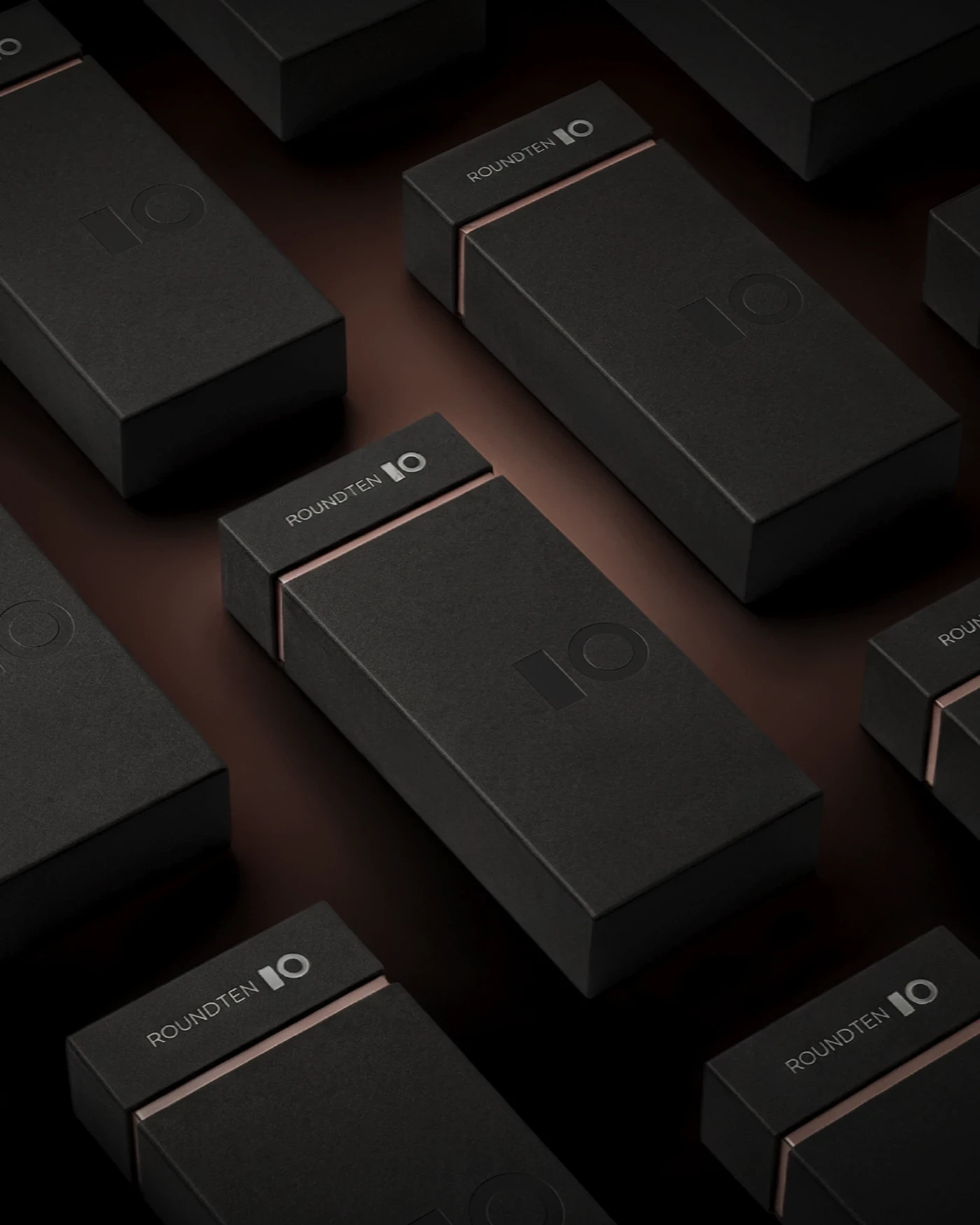 Black Roundten boxes with bronze detailing arranged diagonally, packaging design by Sebastian Saavedra