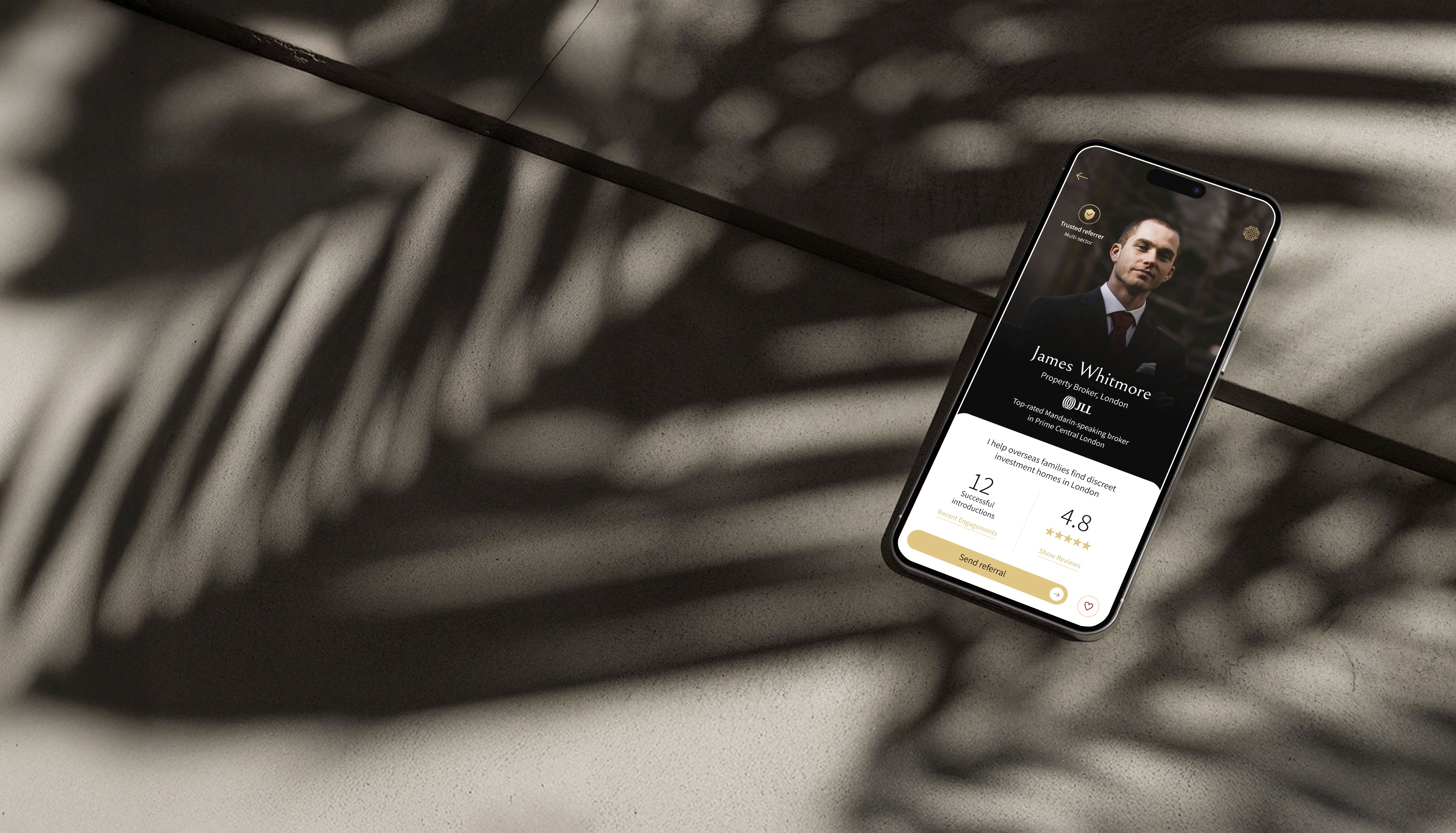 Smartphone lying on a sunlit concrete surface, displaying the East Meets West referral-app profile screen.