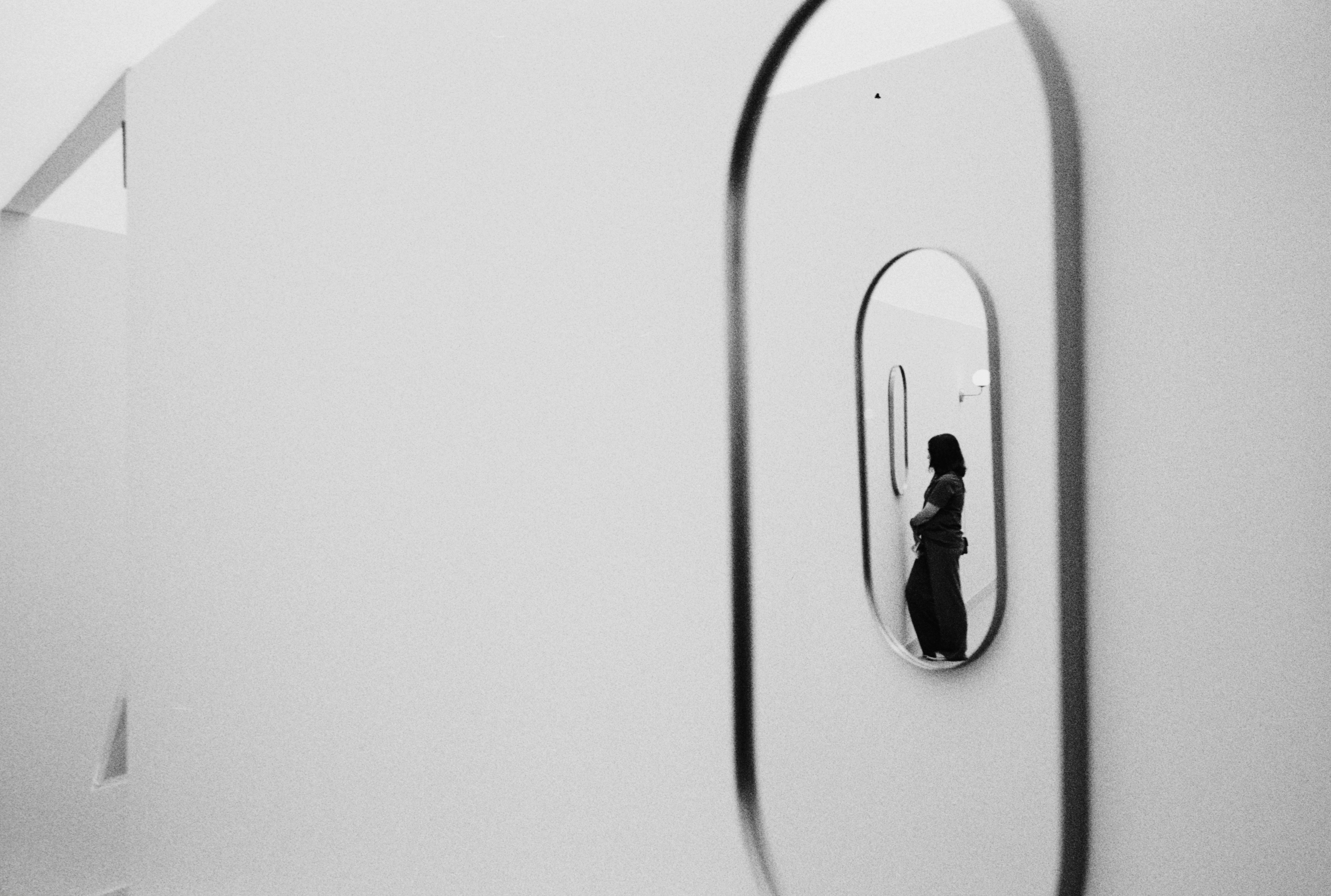 Woman reflected in an oval mirror on a white wall