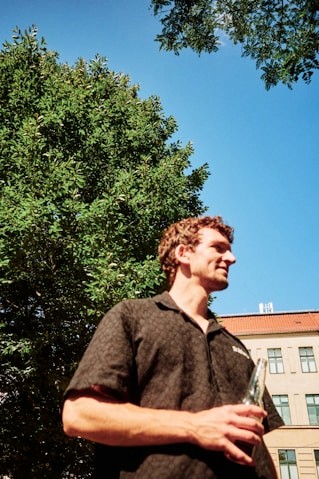 Young man standing outdoors near trees in sunlight