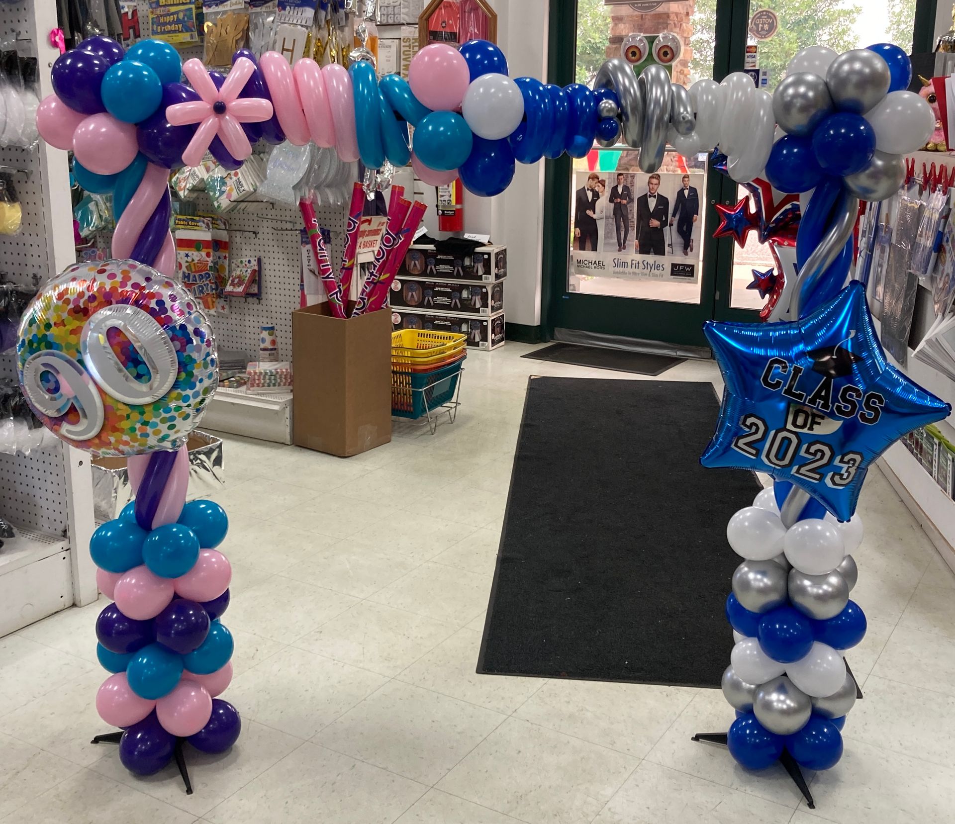 Pair of red, white, and blue spiral balloon columns flanking an entrance for a celebration by Be Bold Balloons
