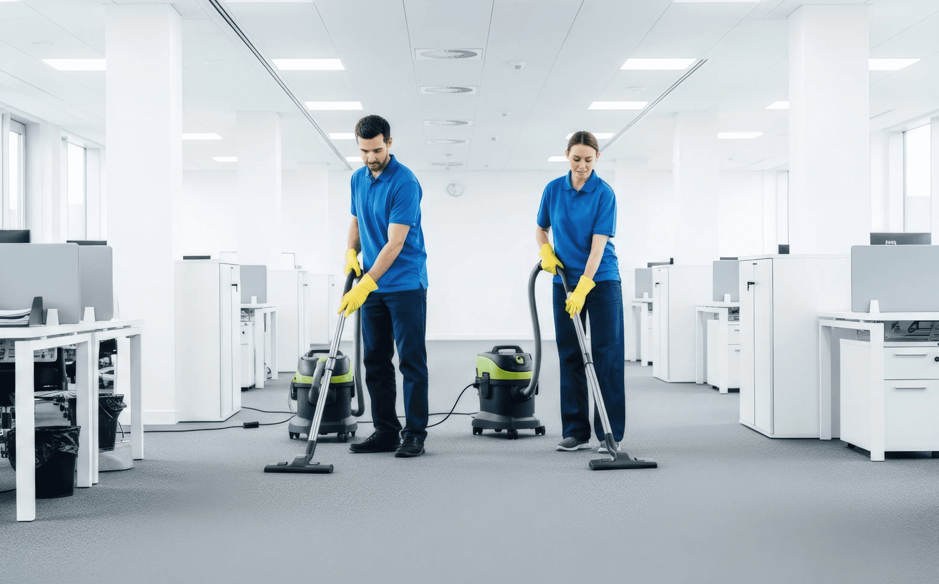 Two janitors using industrial vacuum cleaners to maintain a large, open-plan office space, highlighting professional commercial cleaning solutions.