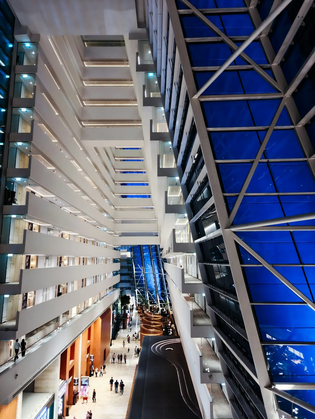 Along the hotel atrium, white balconies on one side and the blue glass wall on the other