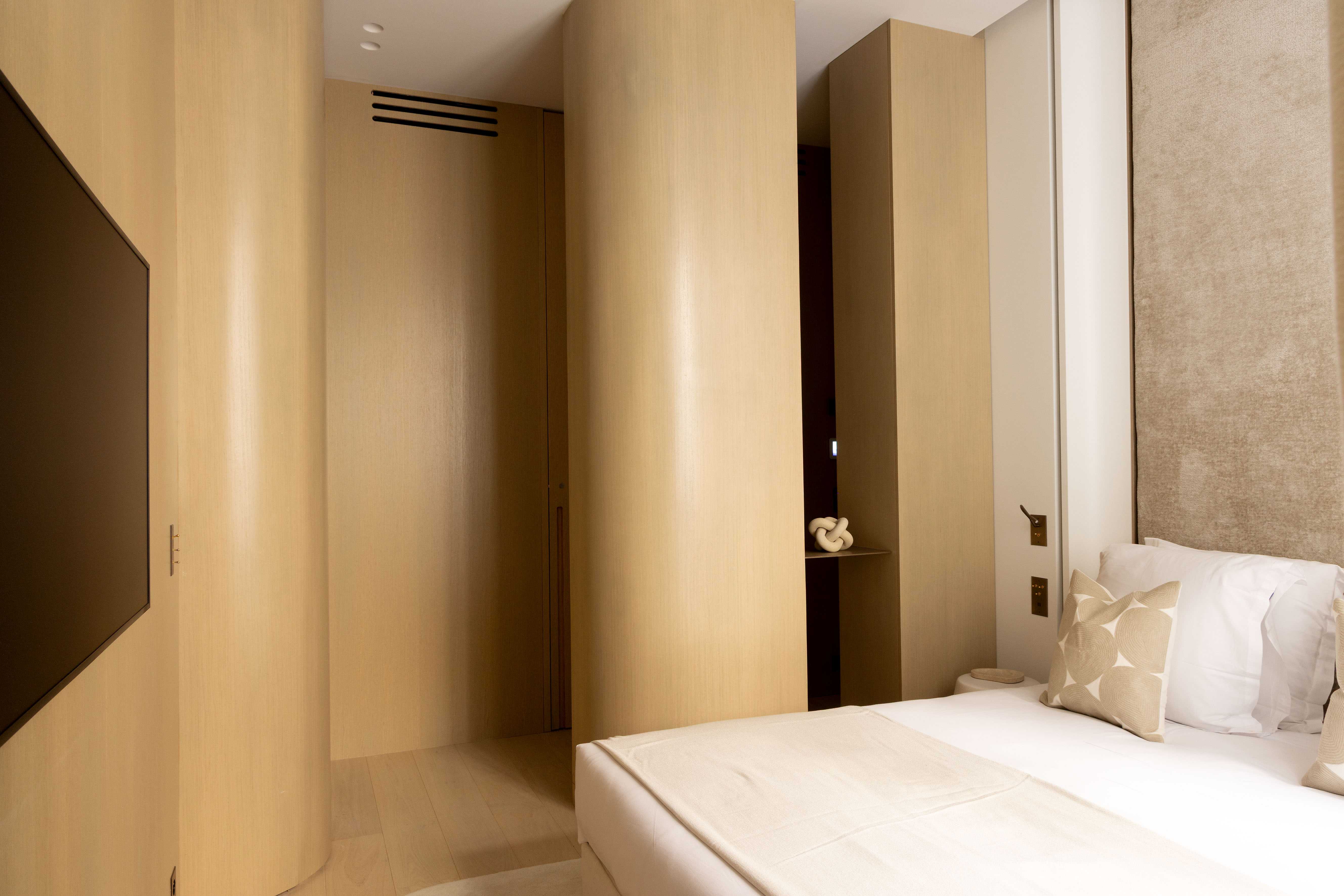 Chambre avec habillage mural en bois clair, télévision encastrée et objet décoratif noeud beige